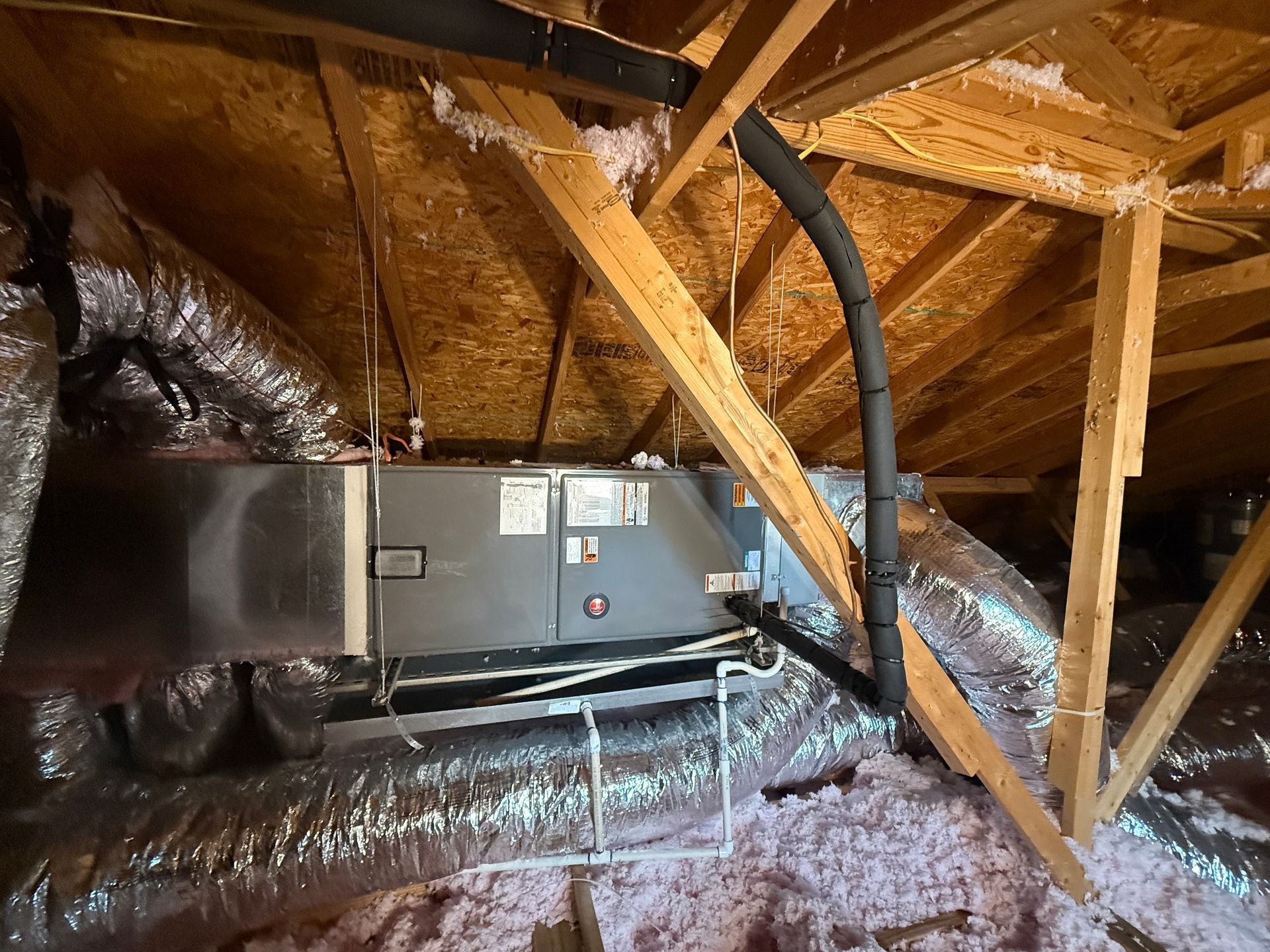 Attic with HVAC unit, ductwork, and wooden framing under sloped roof insulation