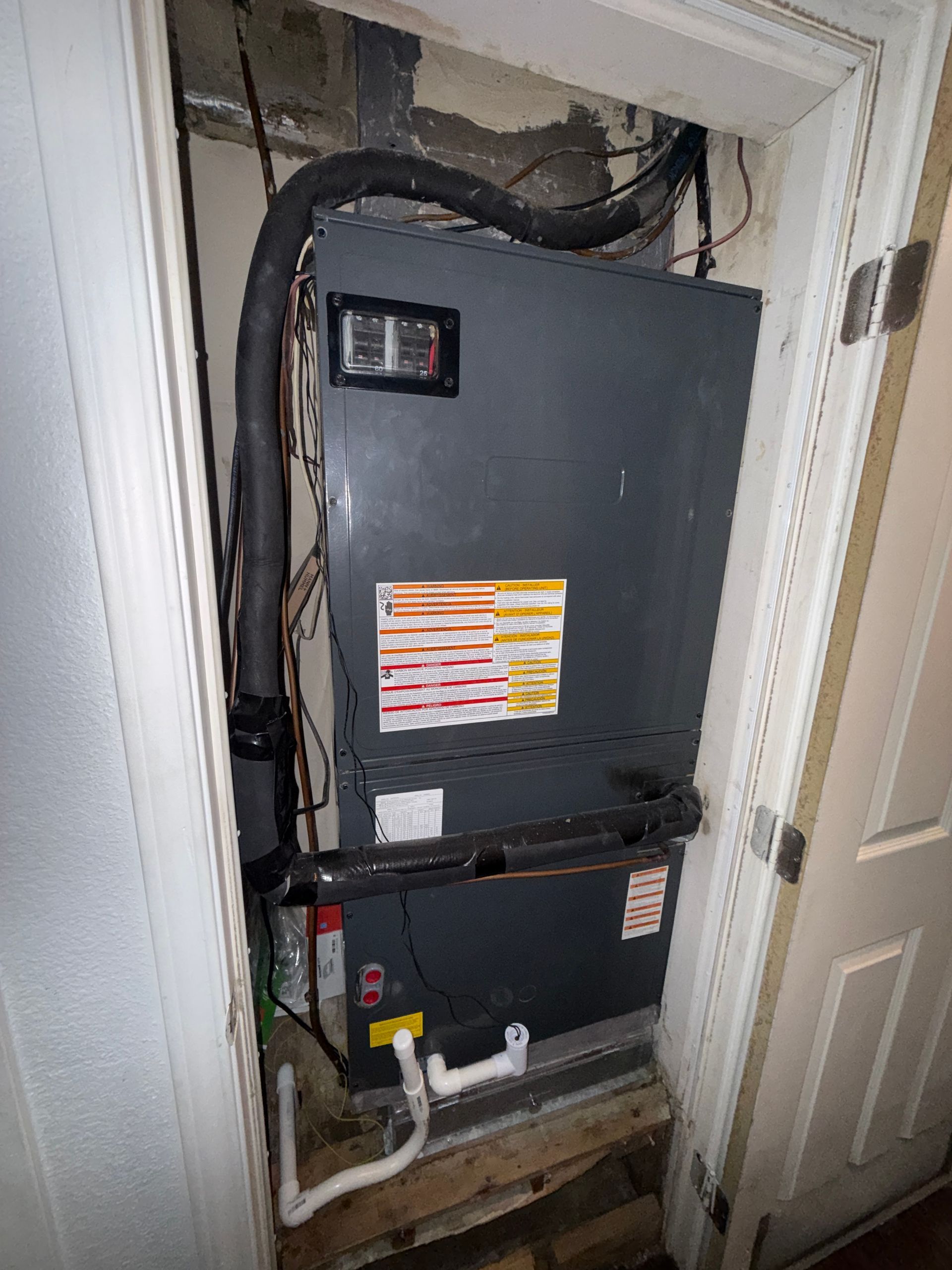 Open utility closet with a large gray HVAC/air handler unit and exposed pipes and wiring.
