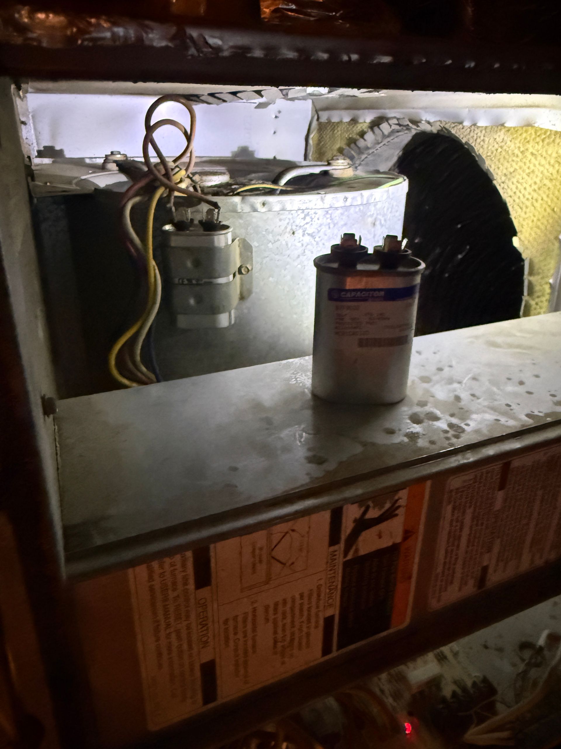 Under-sink cabinet with plumbing, a water filter canister, and a metal shelf in a dimly lit space