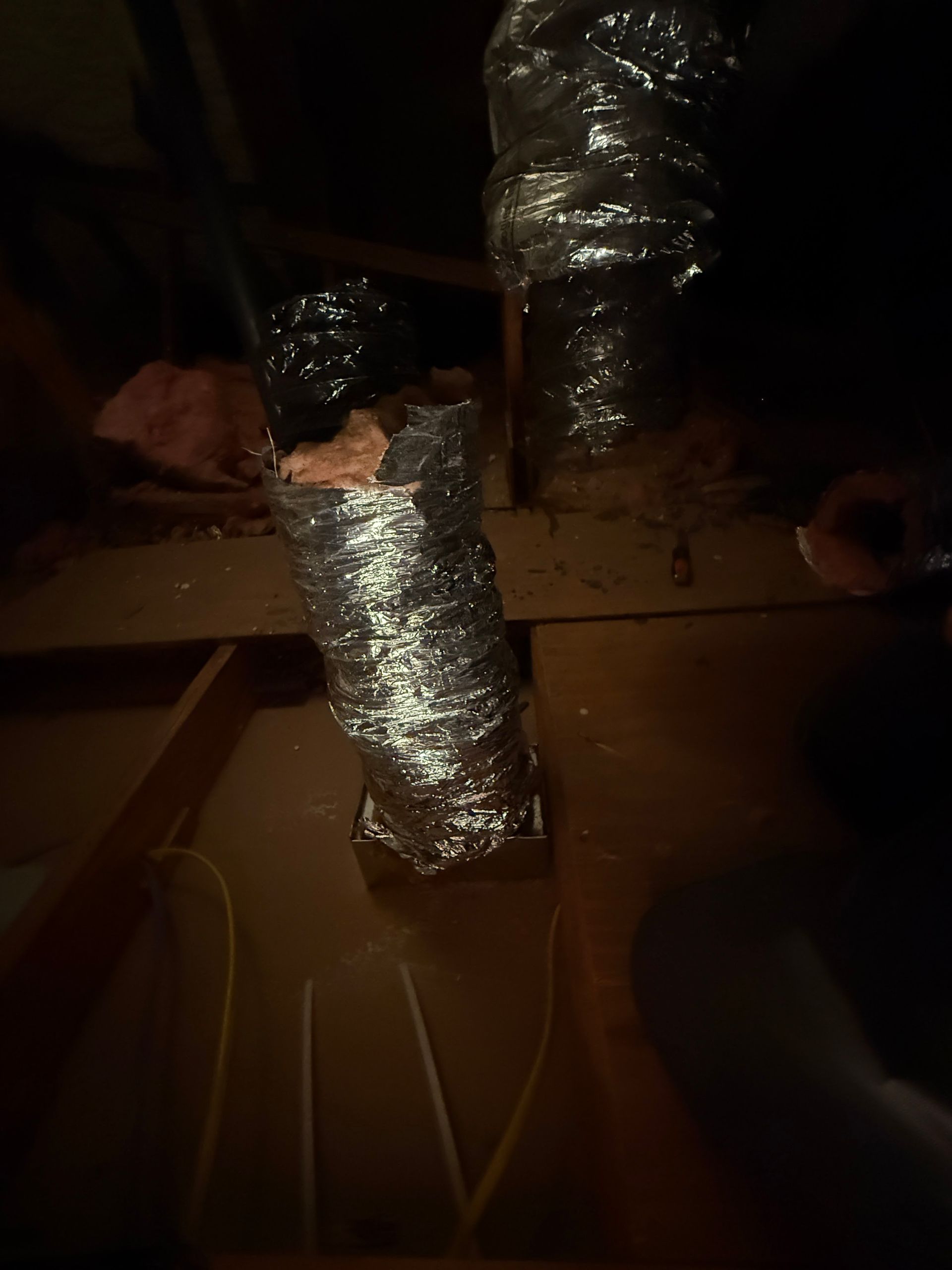 Insulated silver ductwork hanging from a dim ceiling above cardboard boxes and wires