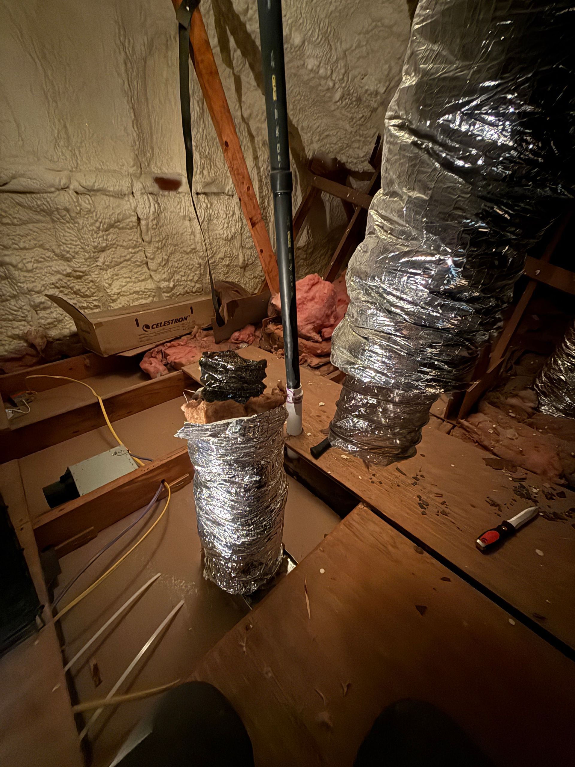 Attic with exposed insulation and HVAC ducts, cardboard boxes, and tools on a plywood floor.
