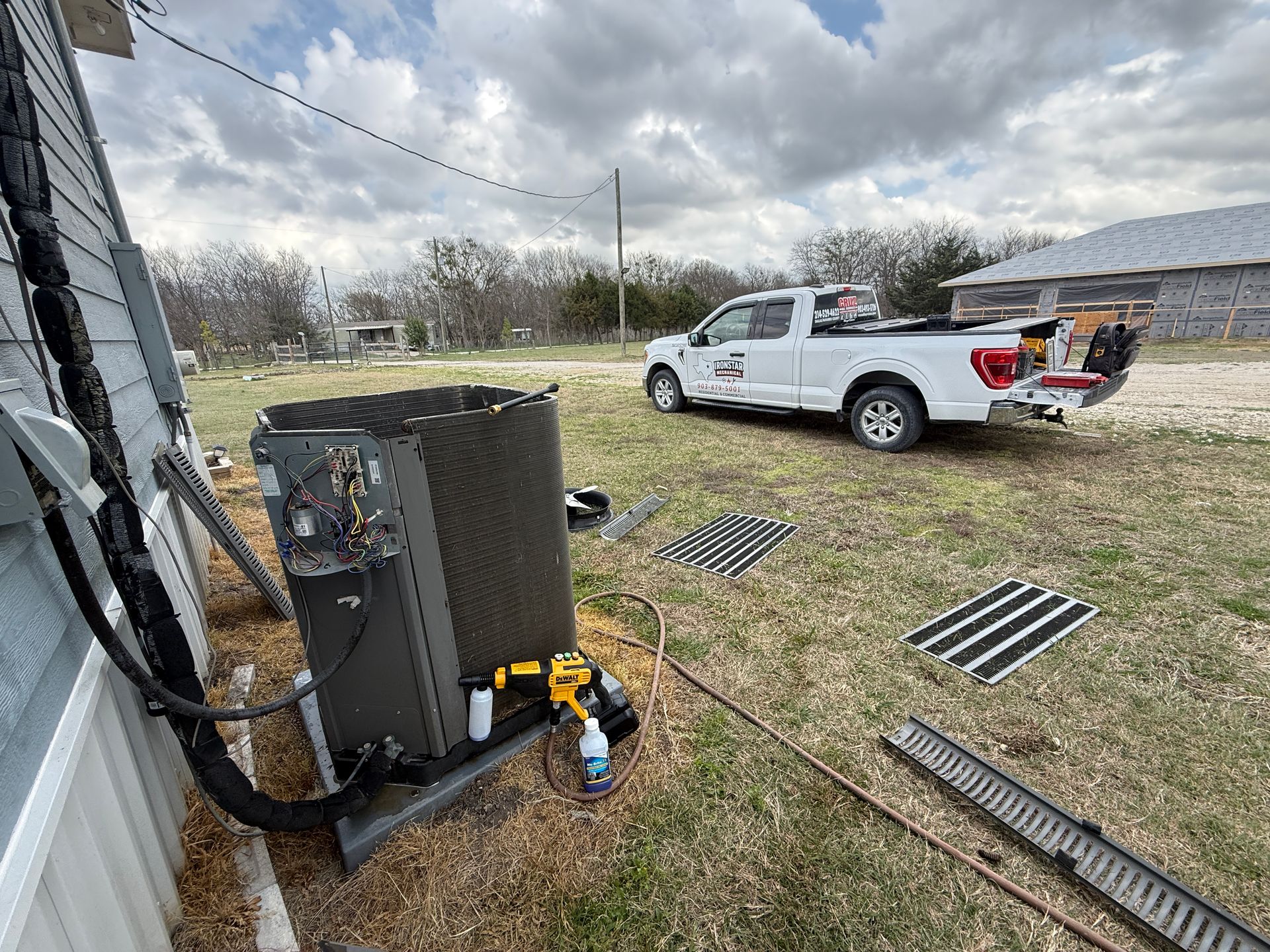 HVAC unit beside a house with a white work truck and metal grates on a grassy yard