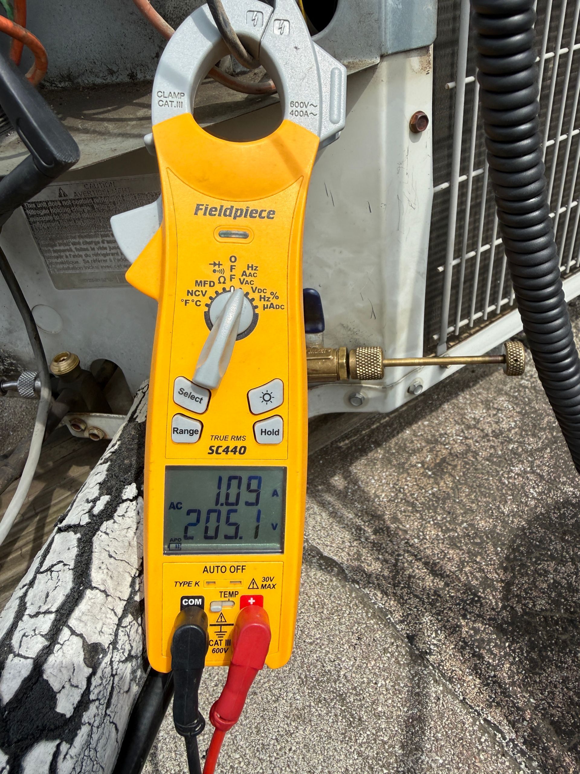 Yellow Fluke clamp meter measuring electrical current outdoors, with red and black probes attached.