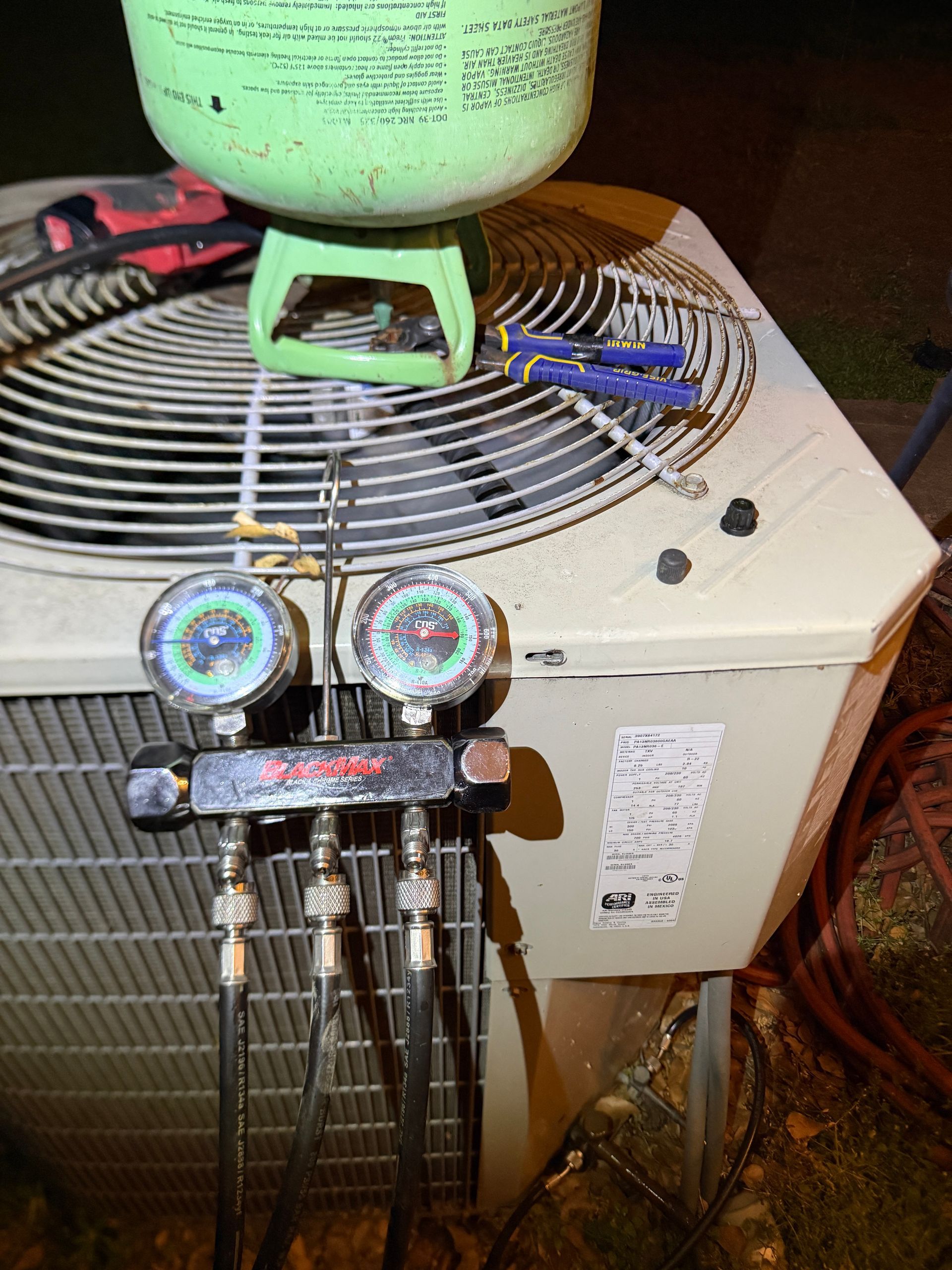HVAC manifold gauges attached to an air conditioner unit with a green refrigerant tank on top