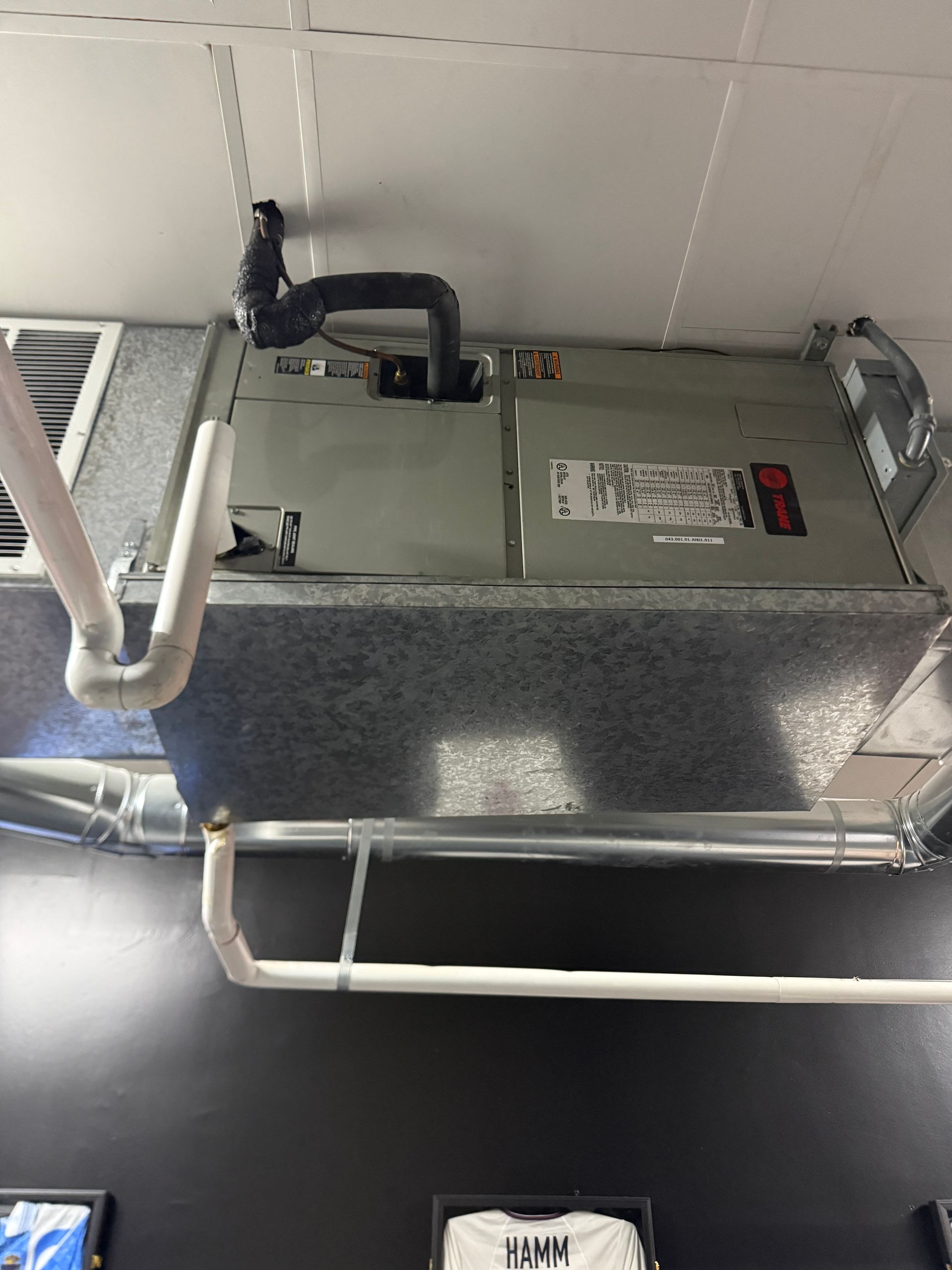Ceiling-mounted HVAC unit with exposed pipes and ductwork in an indoor utility area.