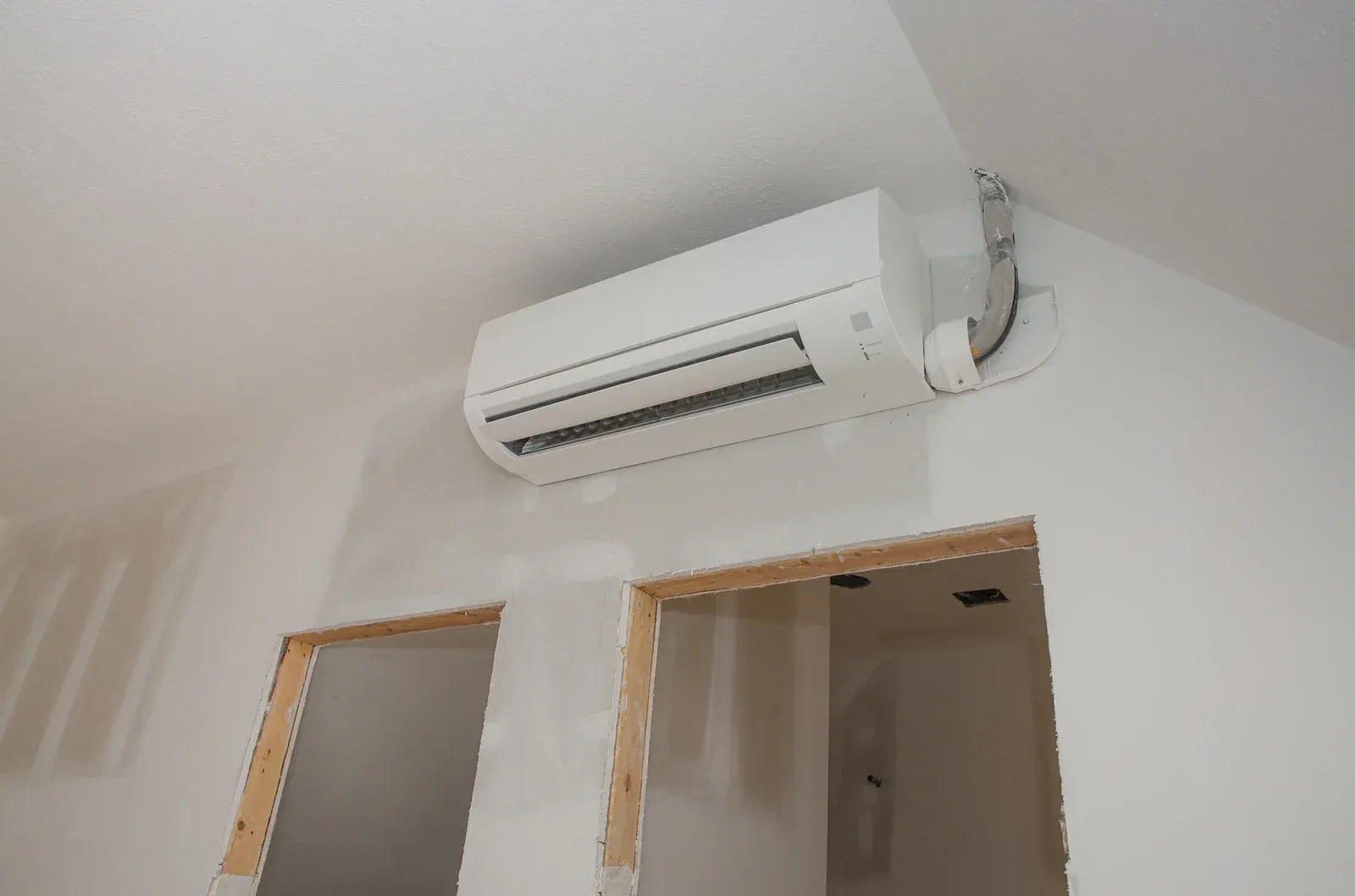 Wall-mounted white air conditioner above two open doorways in a room with white walls