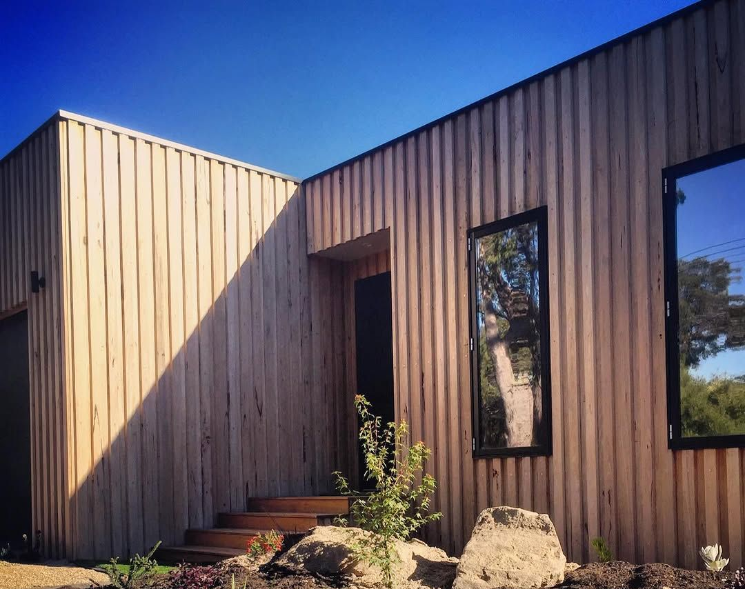Modern wooden building with vertical siding, dark framed windows, and a doorway under a clear blue sky.