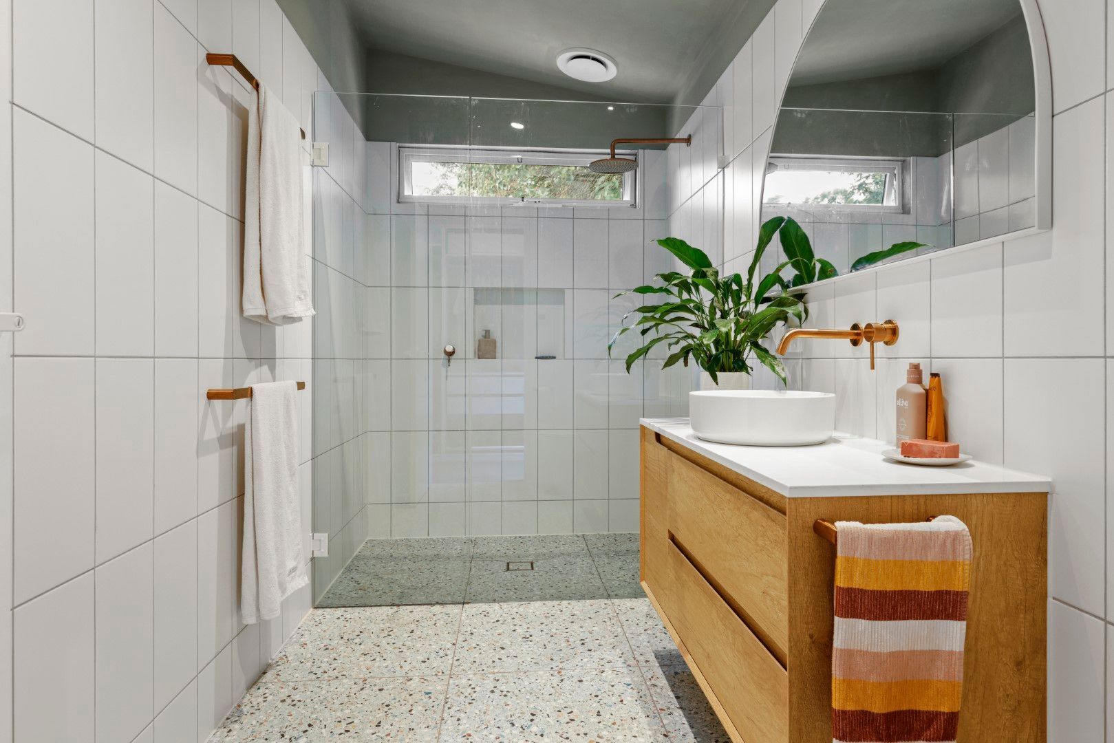 Modern bathroom with white tile, wooden vanity, and glass shower.