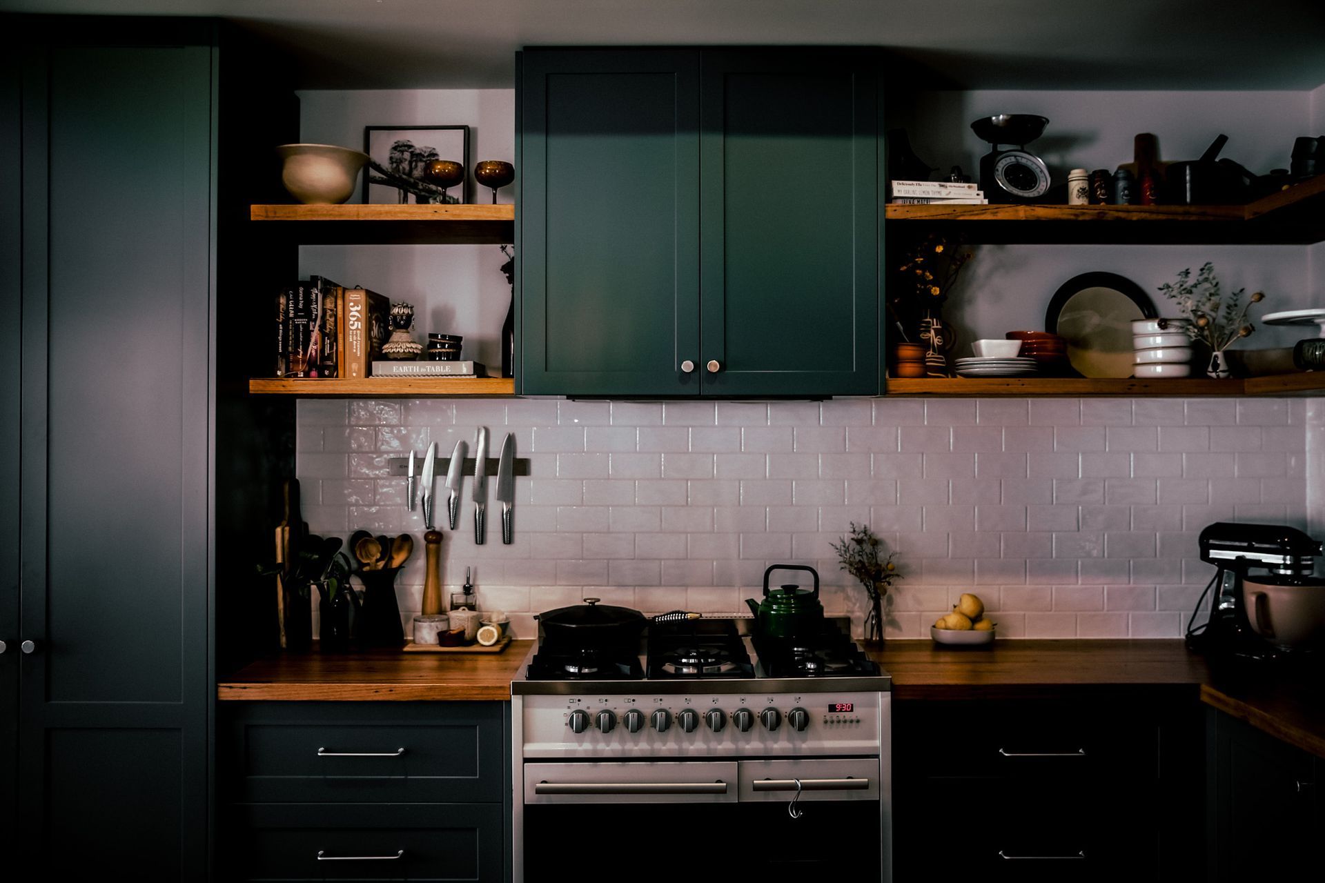 Dark green kitchen with open shelving, stove, and light tiled backsplash.