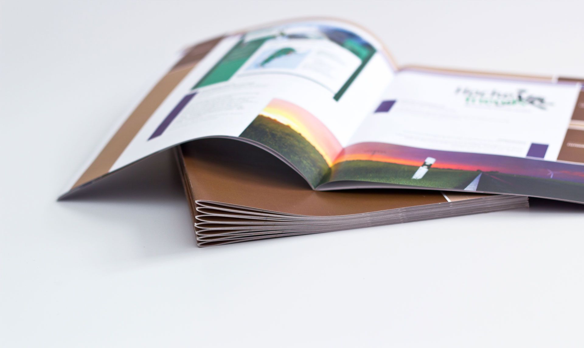 An open brochure with a sunset-themed graphic resting on a stack of brown corrugated cardboard sheets against white.