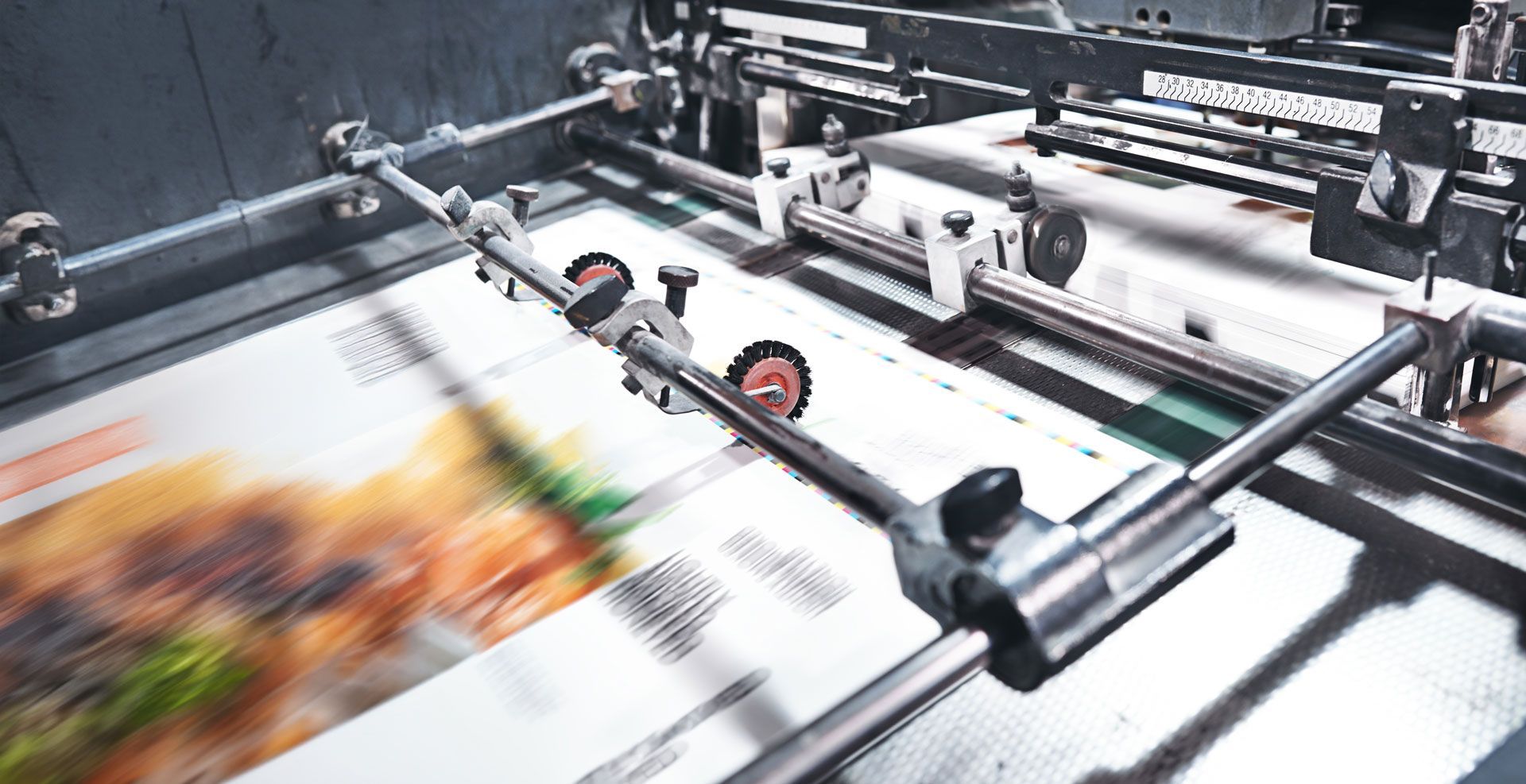 Printed materials moving through a commercial printing press with metal rollers and guides.