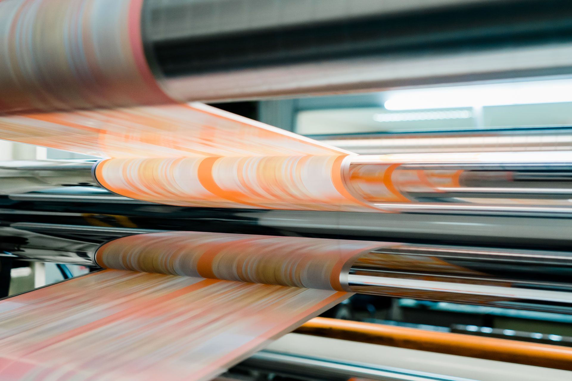 A thin, light-colored film moving through industrial rollers in a manufacturing facility.