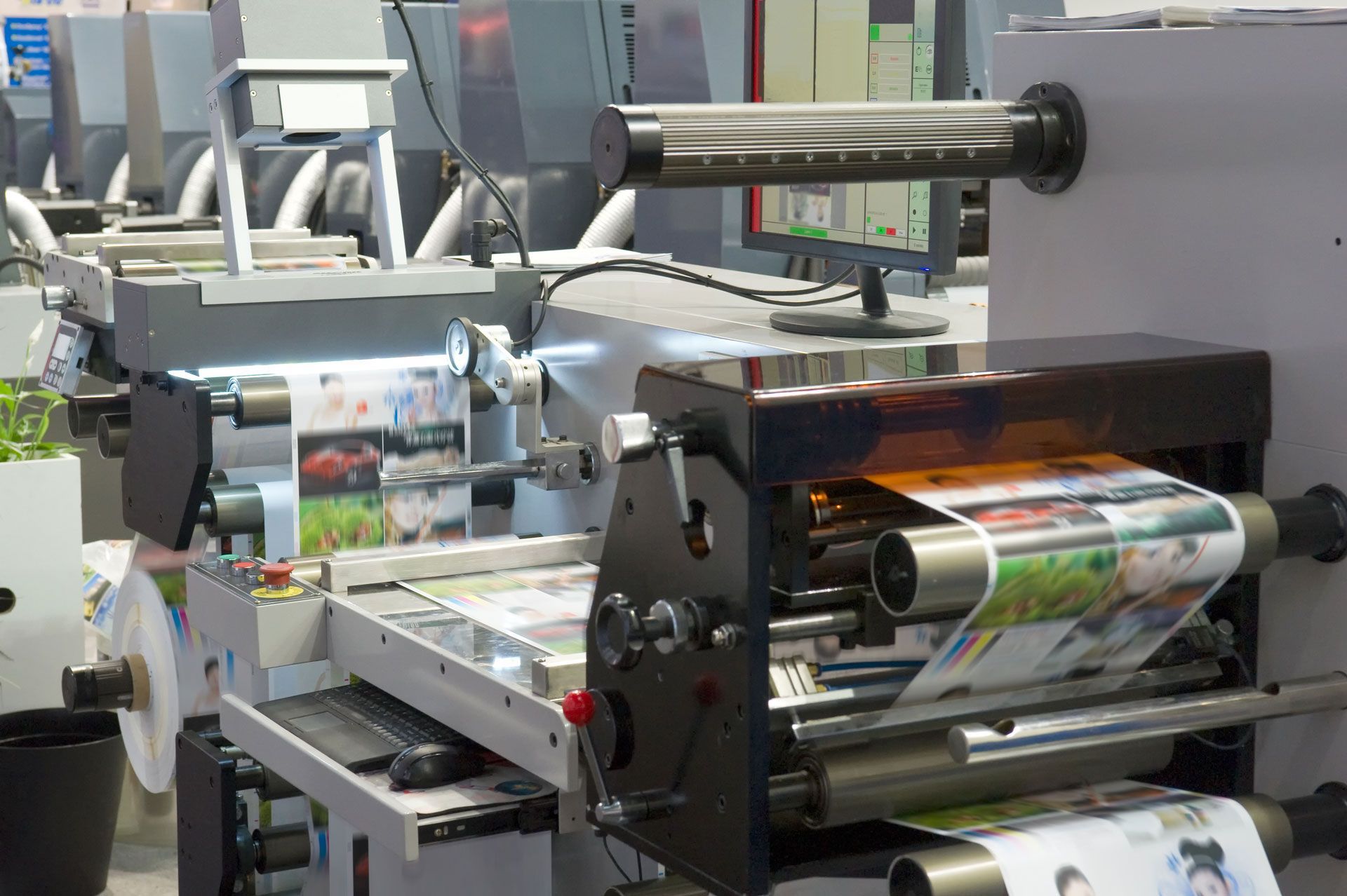 Industrial printing press machine with a continuous paper roll moving through rollers in a production facility.