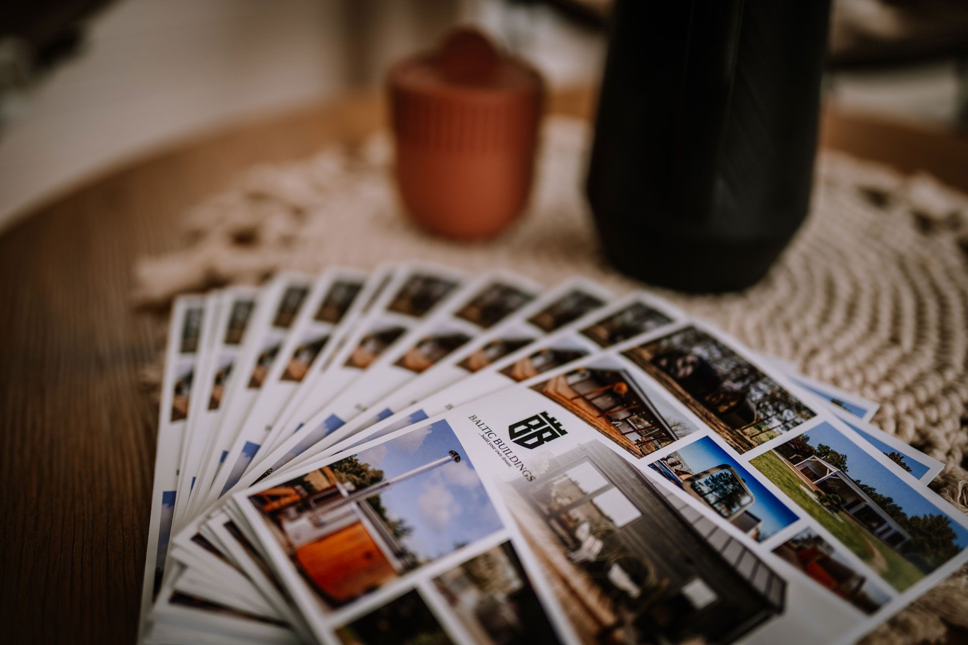 A fan of printed brochures featuring photos of modern cabins and houses lies on a wooden table beside a dark vase.