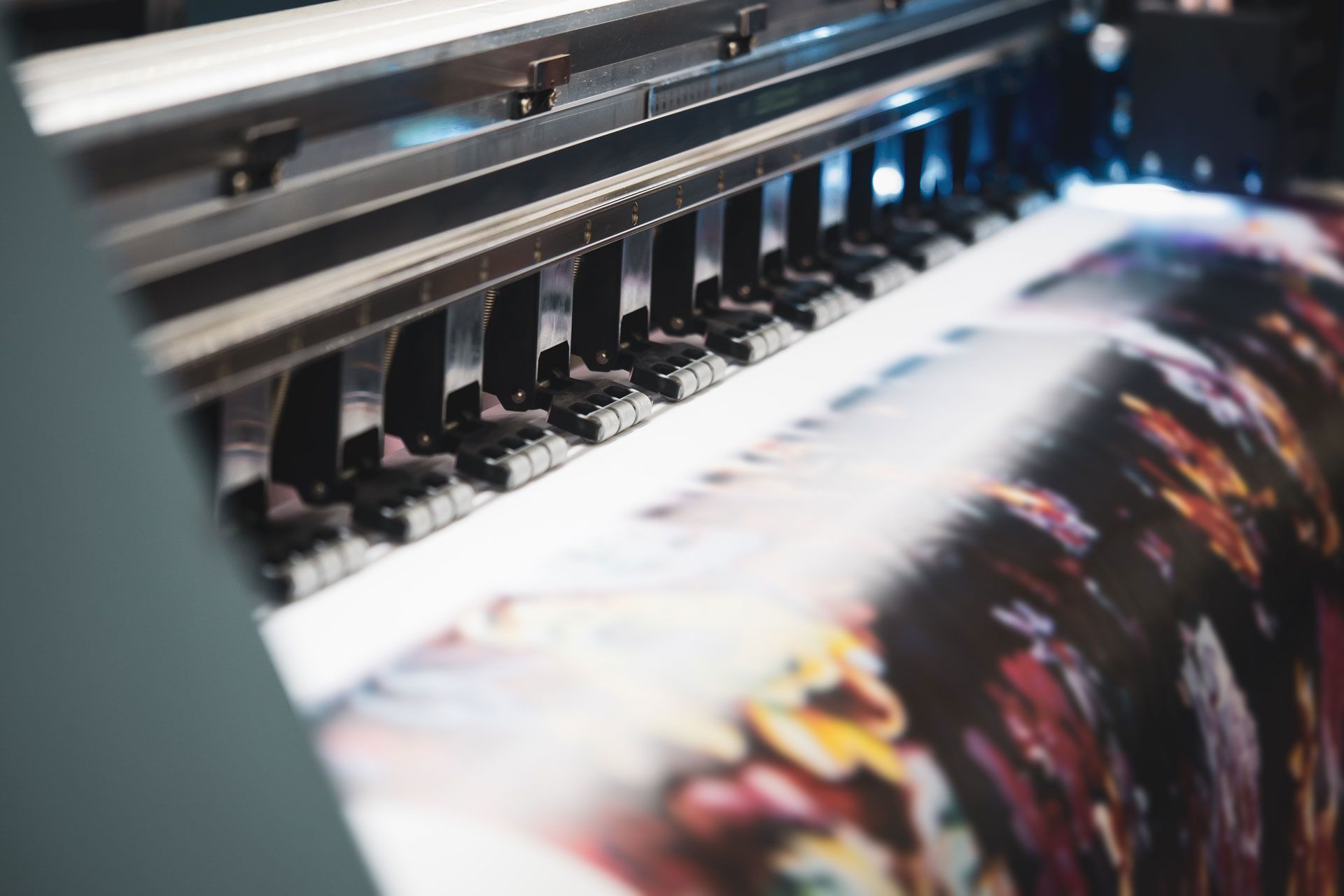 A large-format industrial printer head depositing colorful ink onto a roll of paper.