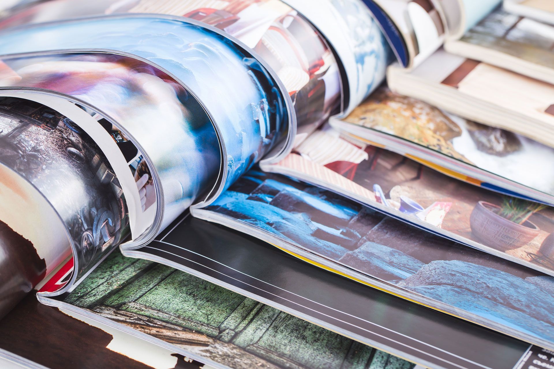 A close-up view of several stacked magazines with curled pages showcasing colorful photography and artistic layouts.