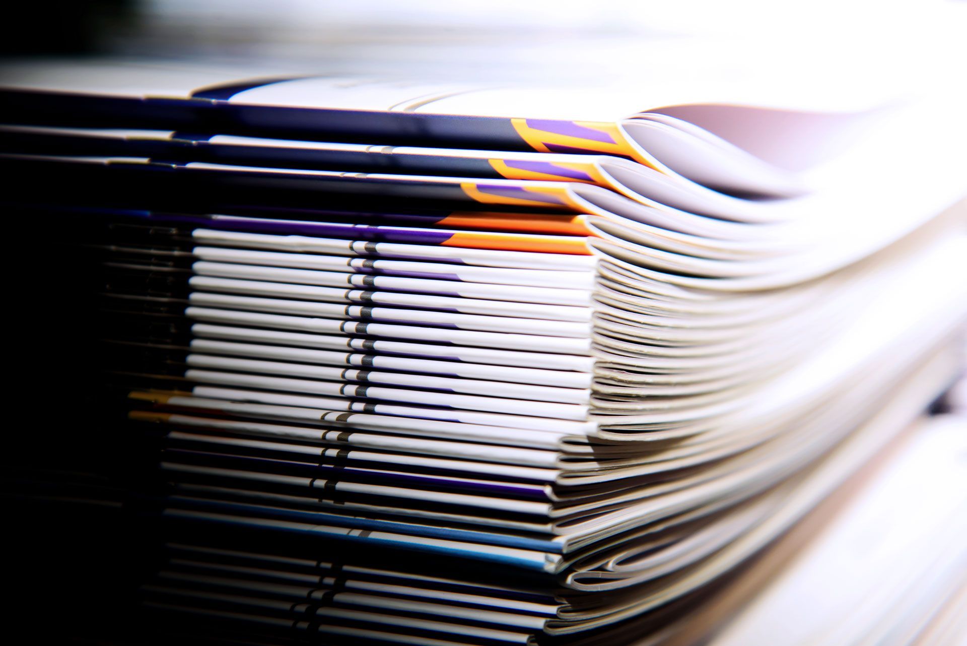 A close-up, angled view of a neat stack of documents and brochures with colorful branding along their spines.