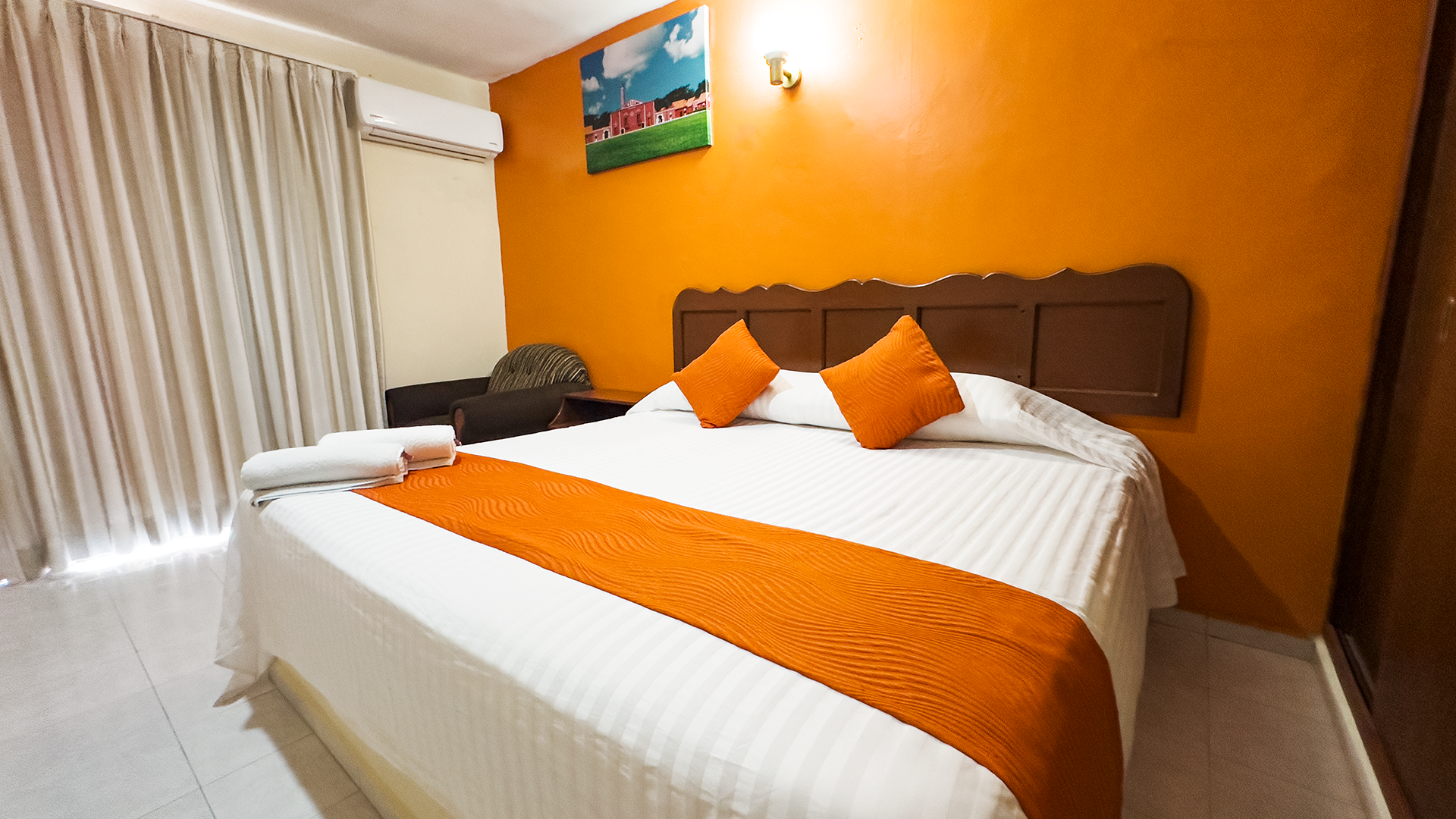 A hotel room with a queen bed featuring a white striped comforter.