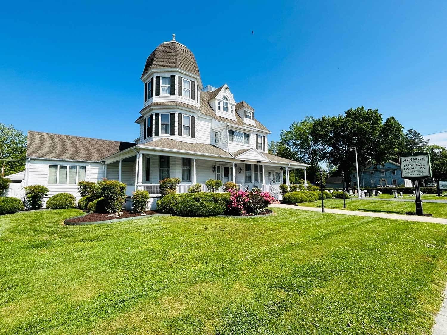 White Victorian house with a domed turret, surrounded by green grass and bushes, sunny day.