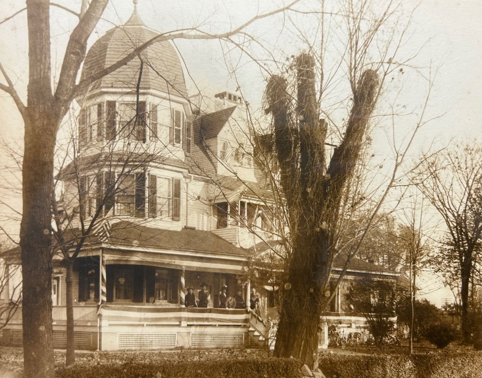 Vintage, three-story Victorian house with a domed turret, large porch, and bare trees in front.