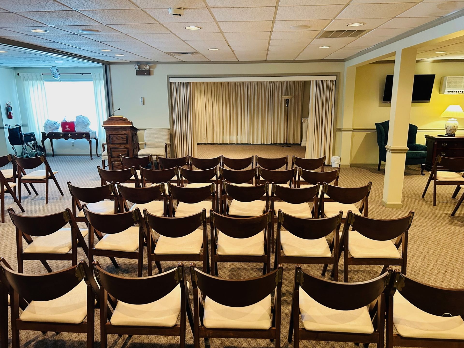 Rows of brown chairs face a stage with closed curtains in a room.