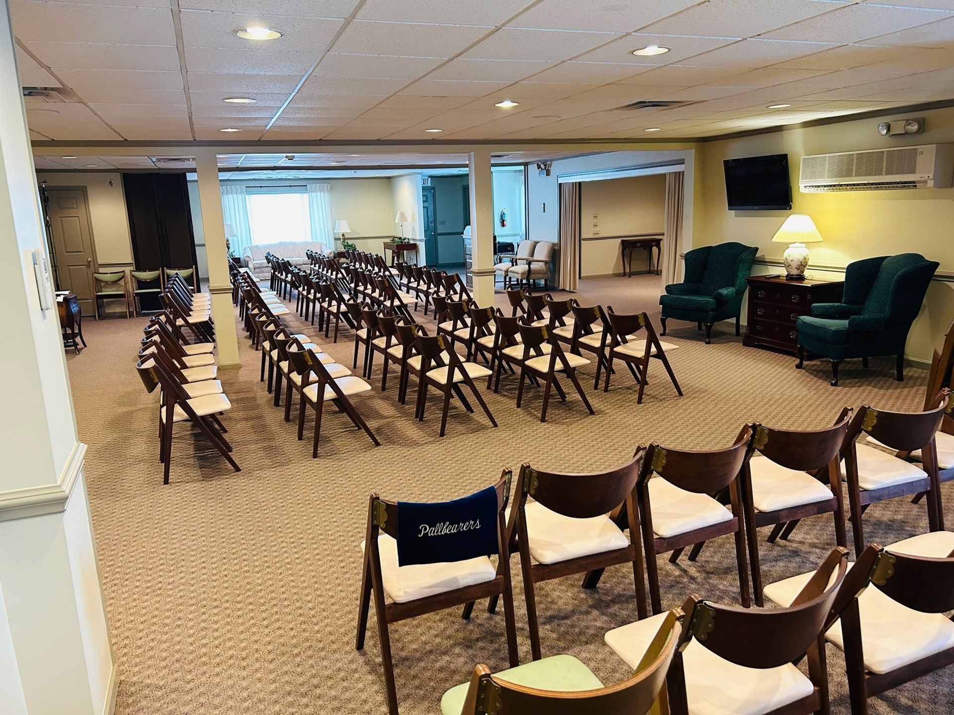 Rows of folding chairs face an open space in a carpeted room, with seating areas on the sides.