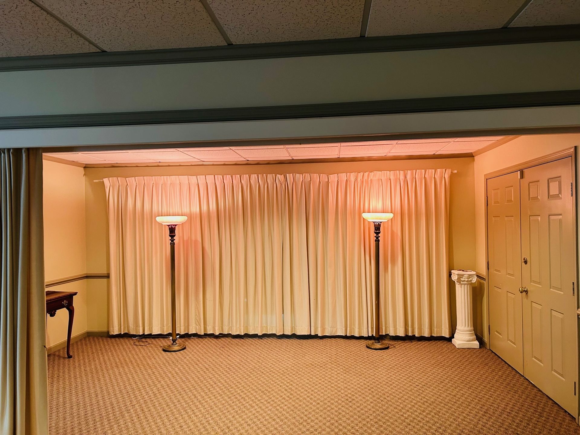Interior room with ivory curtains, two lamps, and a closed door. Beige carpet and yellow walls.