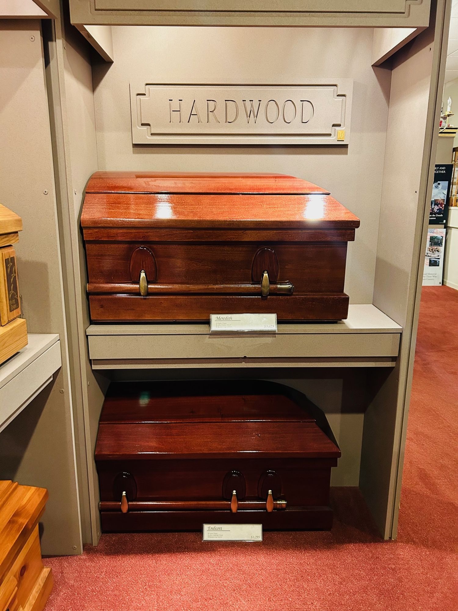 Two wooden hardwood coffins on display in a store. Both are brown with gold handles.