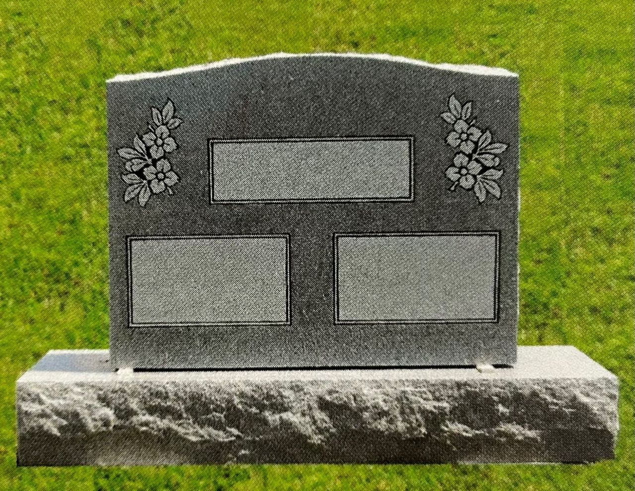 Gray granite tombstone with floral carvings on a green lawn.