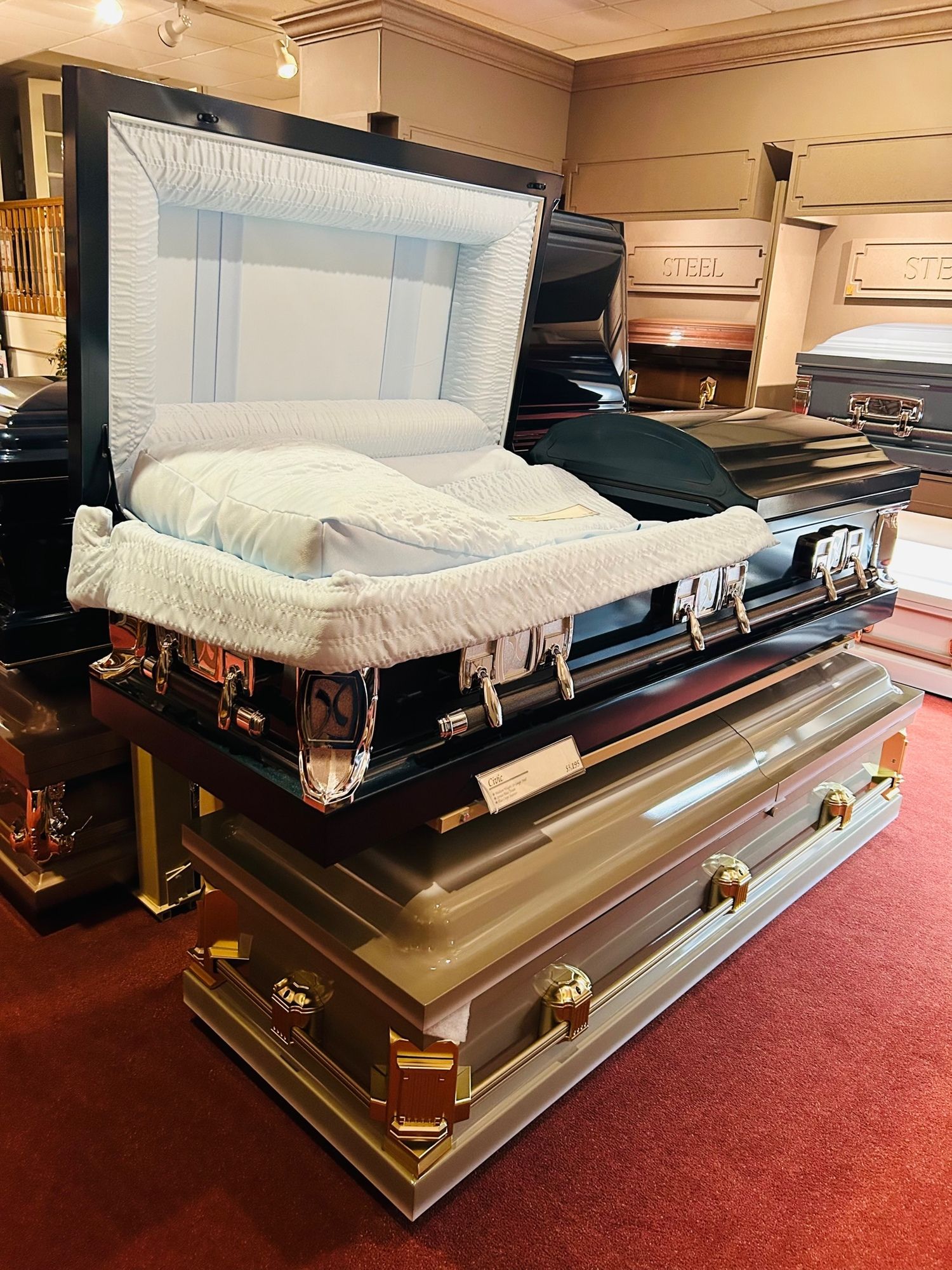 An open black coffin with a white interior, stacked on other closed coffins in a store.