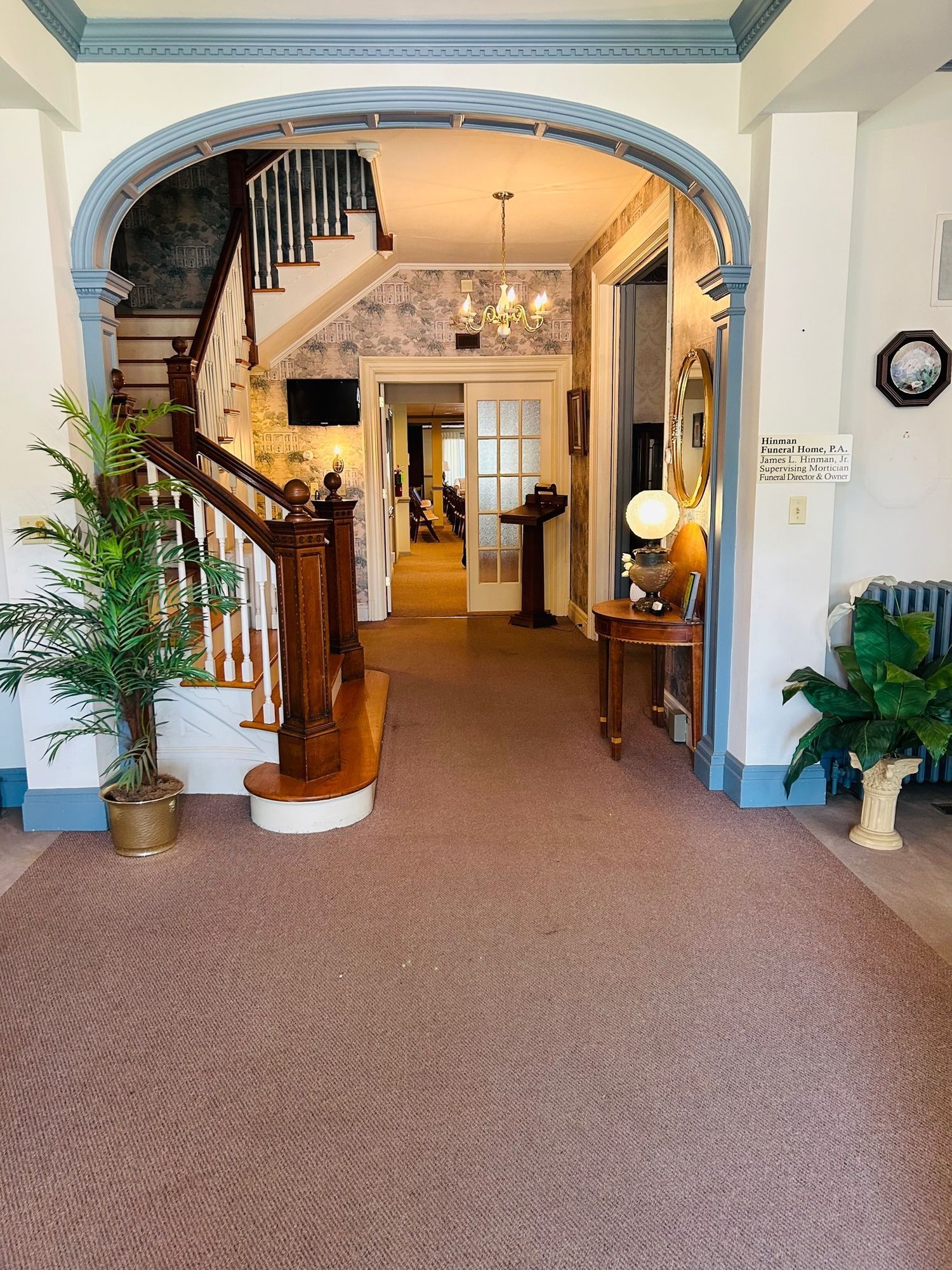 Interior view of a hallway with a staircase. Brown carpet, archway, and wood accents.