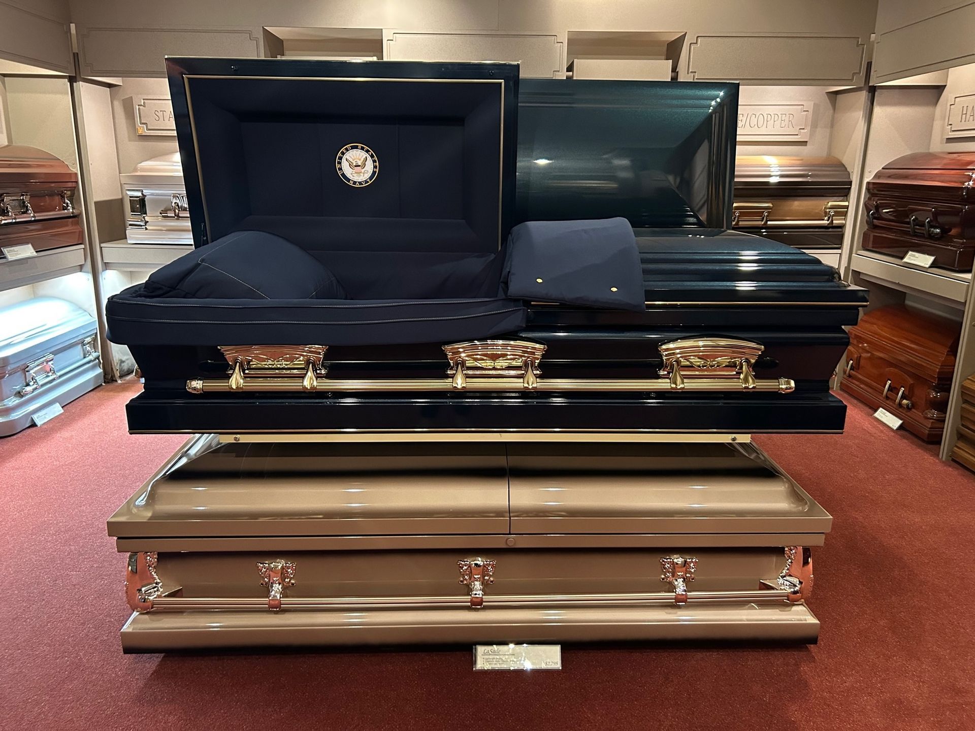 Two open and closed coffins on display in a store, dark blue and bronze with gold handles.