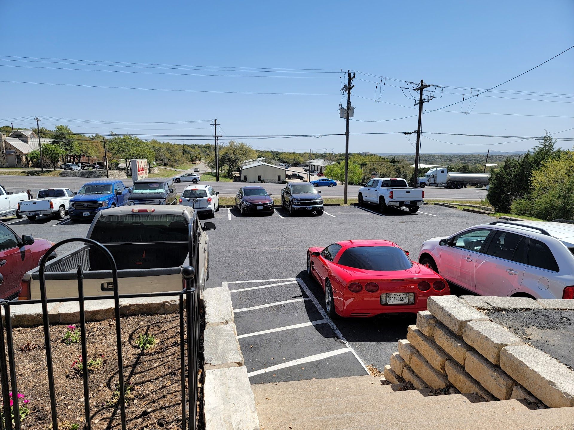 Cars parked in a paved lot, red Corvette in focus, trees and utility pole s visible, blue sky. | QualTech Automotive