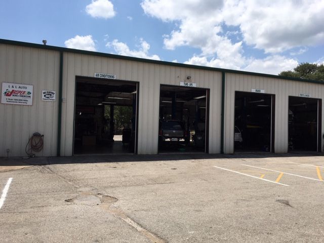 Exterior of a car repair shop with open garage doors and cars inside. The building is beige with a paved area in front. | QualTech Automotive