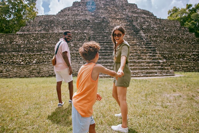 A woman wearing a hat and sunglasses is standing next to a fence.