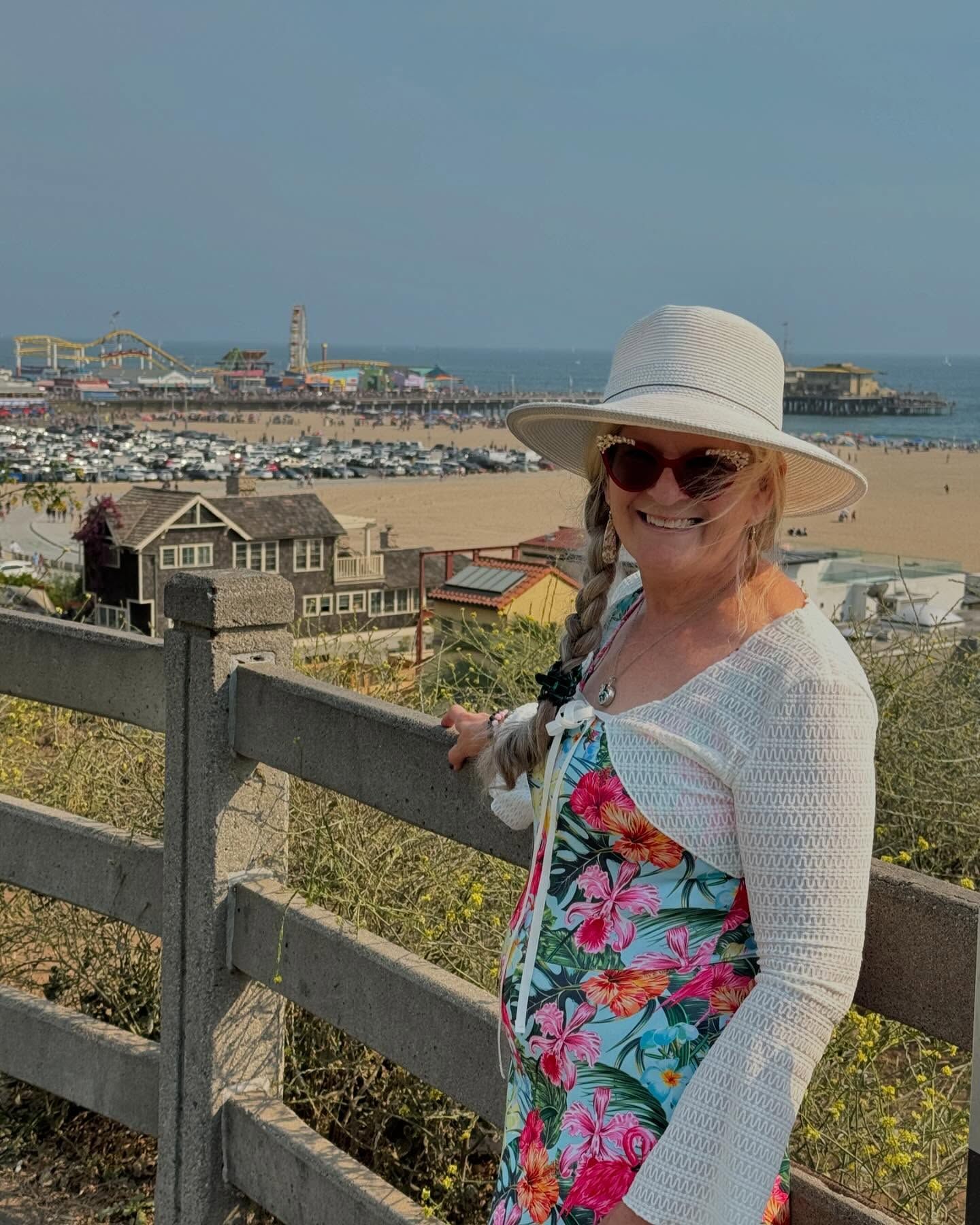 A woman wearing a hat and sunglasses is standing next to a fence.