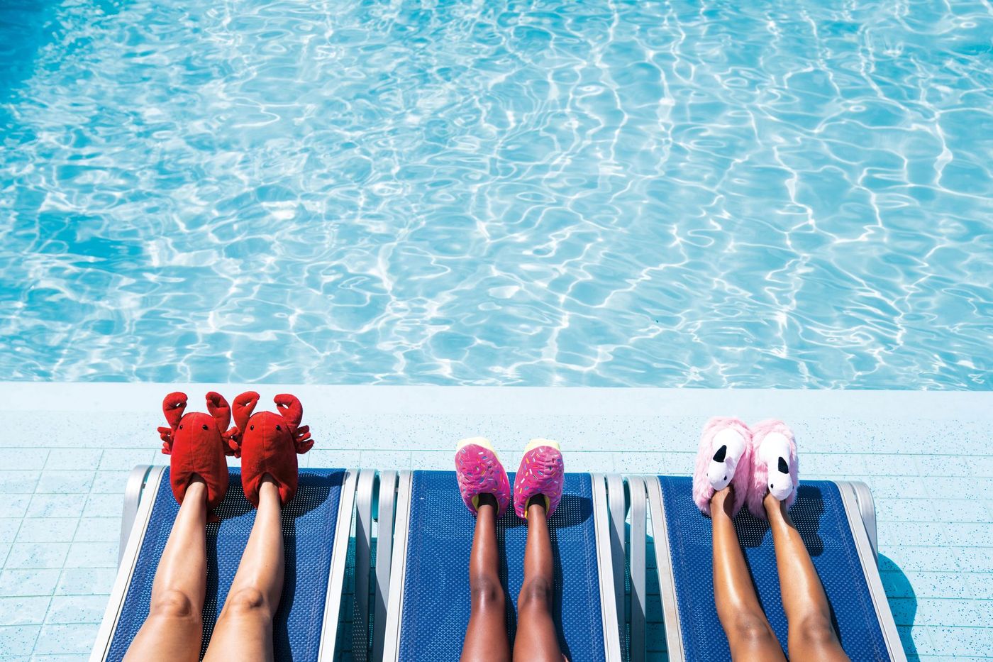 A woman is laying on a towel next to a swimming pool wearing slippers.