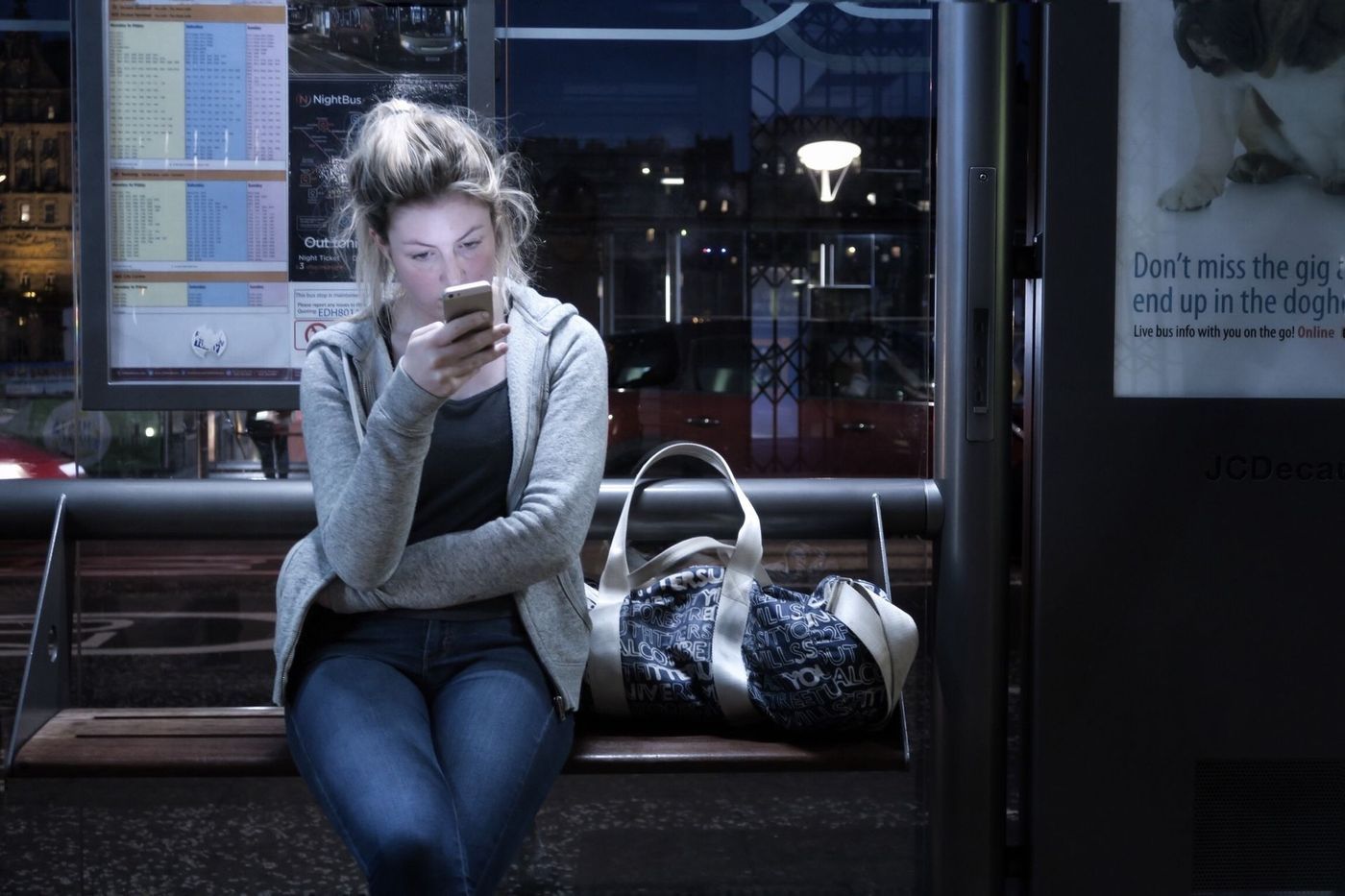A woman is sitting at a bus stop looking at her phone