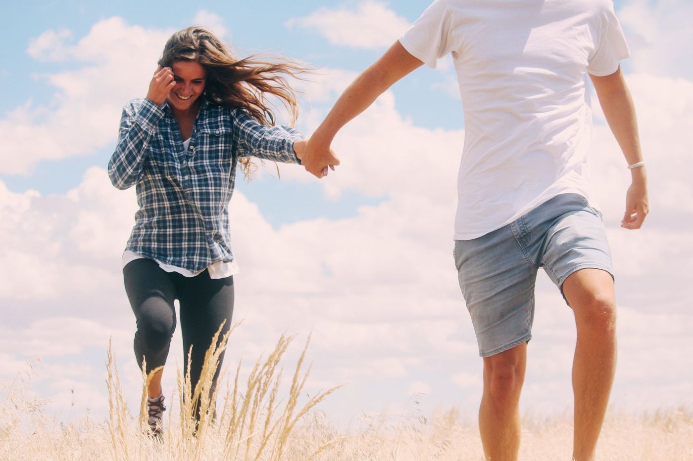A man and a woman are running through a field holding hands.