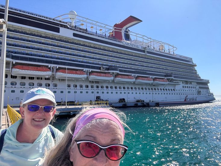 A woman wearing a hat and sunglasses is standing next to a fence.