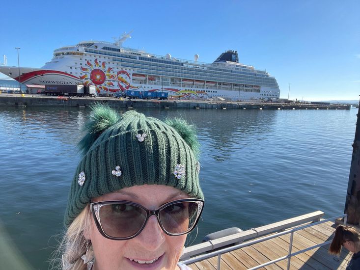 A woman wearing a hat and sunglasses is standing next to a fence.