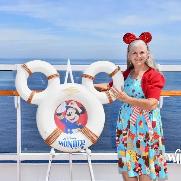 A woman stands in front of a life preserver that says disney wonder