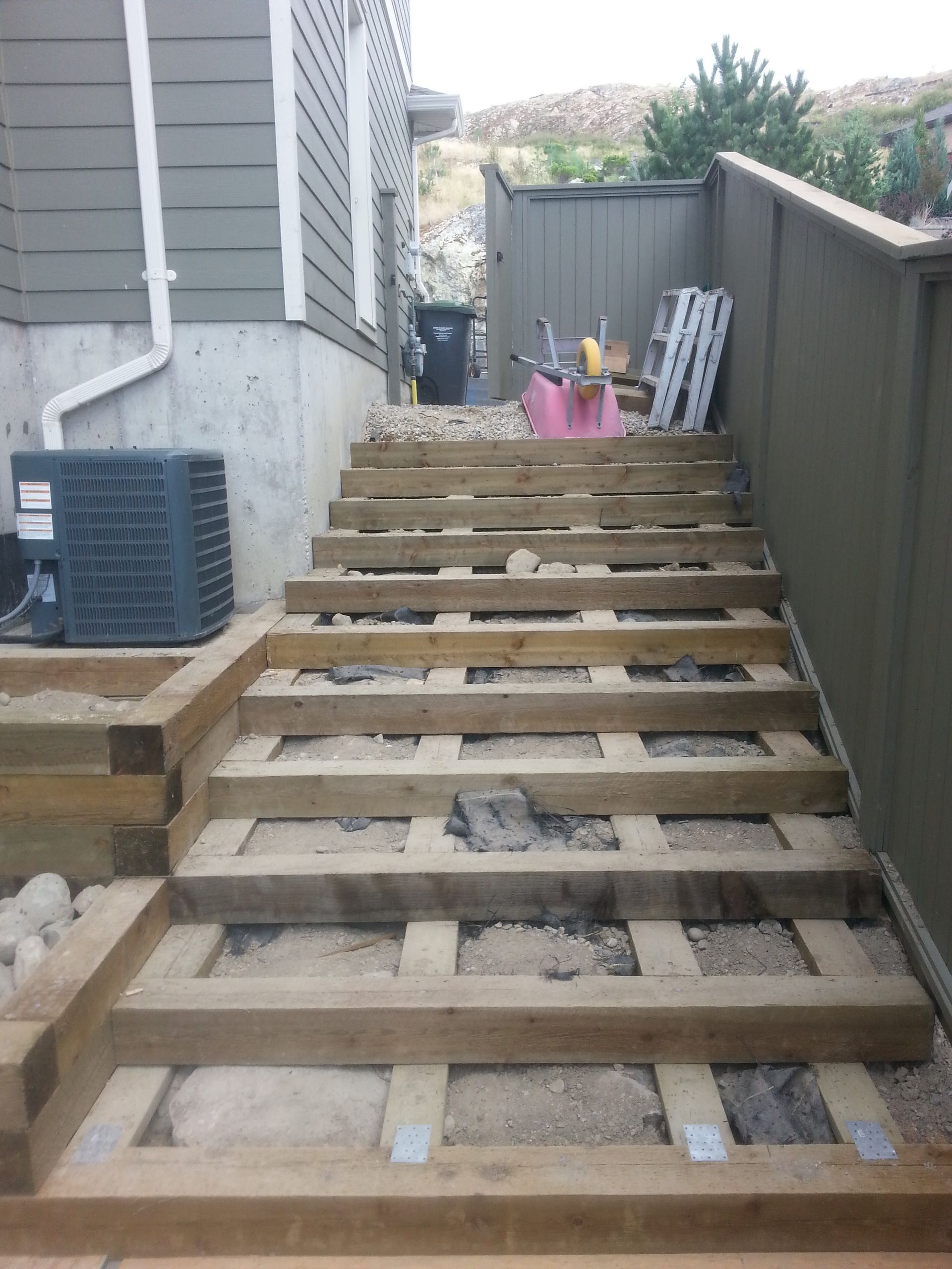 Wooden staircase under construction outdoors near a house; unfinished steps and surrounding area.