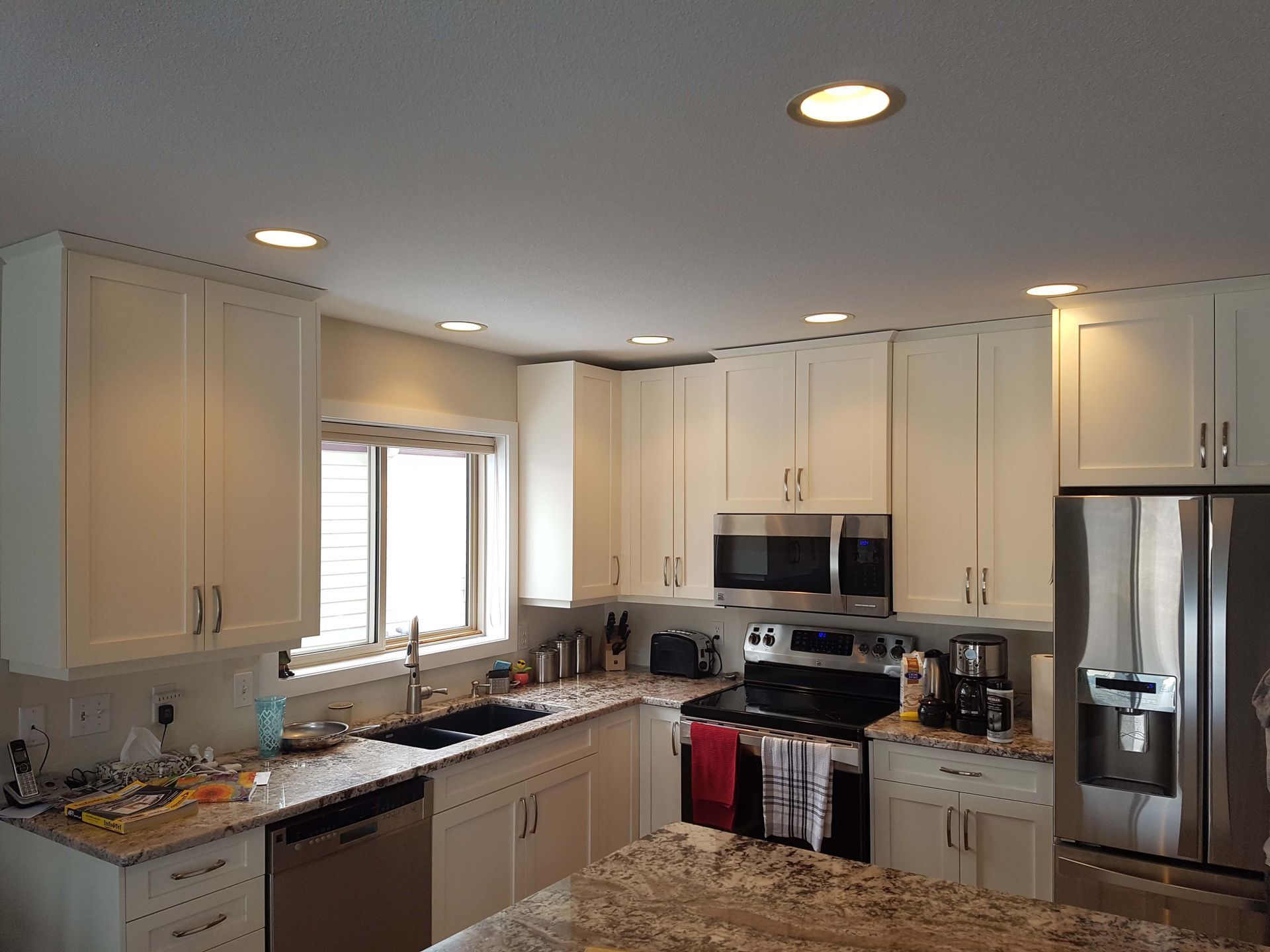 White kitchen with cabinets, appliances, and recessed lighting. Stainless steel refrigerator.