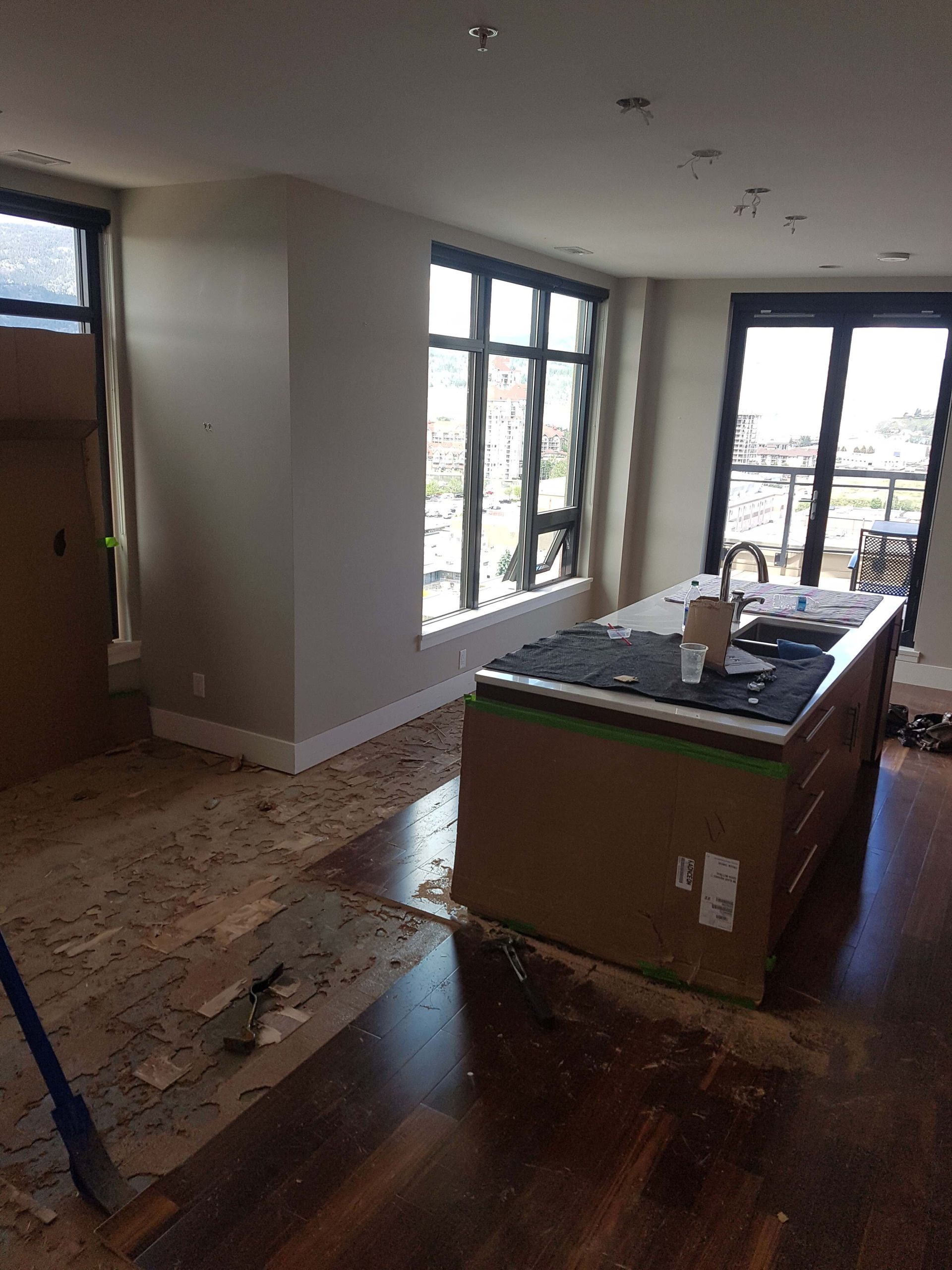 Kitchen under construction: island with black countertop, large windows, wood flooring being removed.