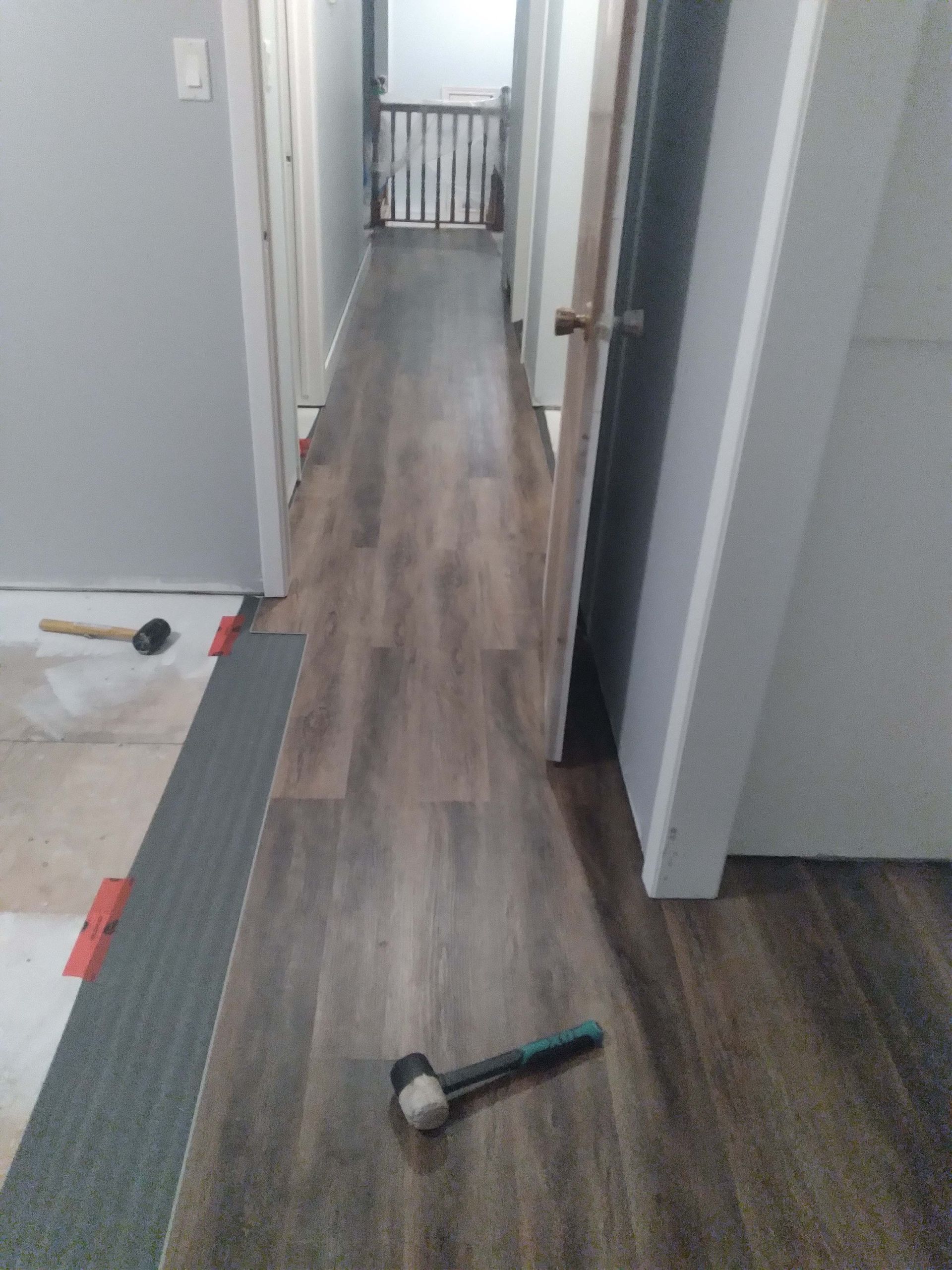 Hallway with dark wood-look flooring being installed, a hammer and tools are on the floor.