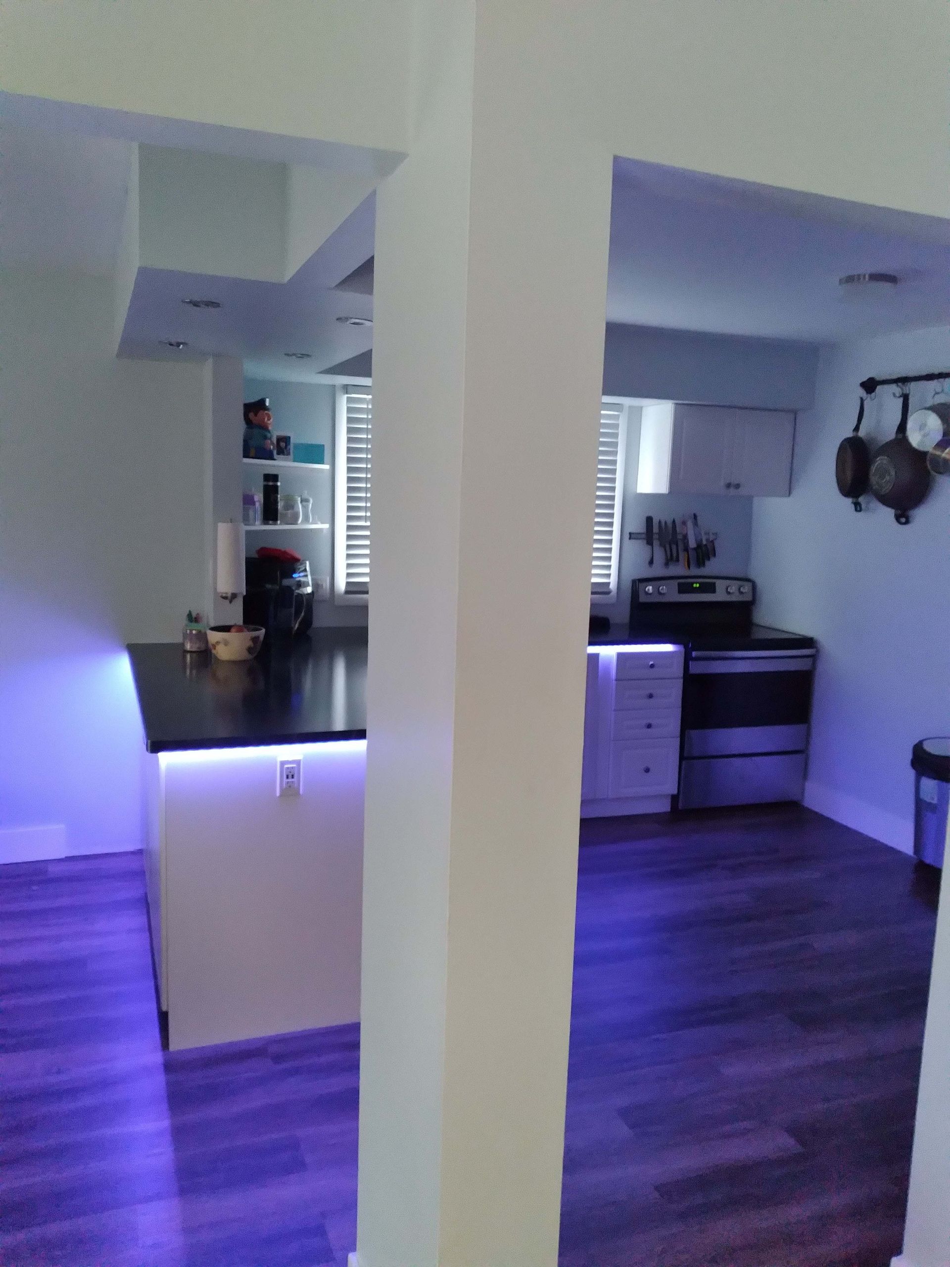 Kitchen interior with a white column separating a dark countertop island and a kitchen with a stove and cabinets.