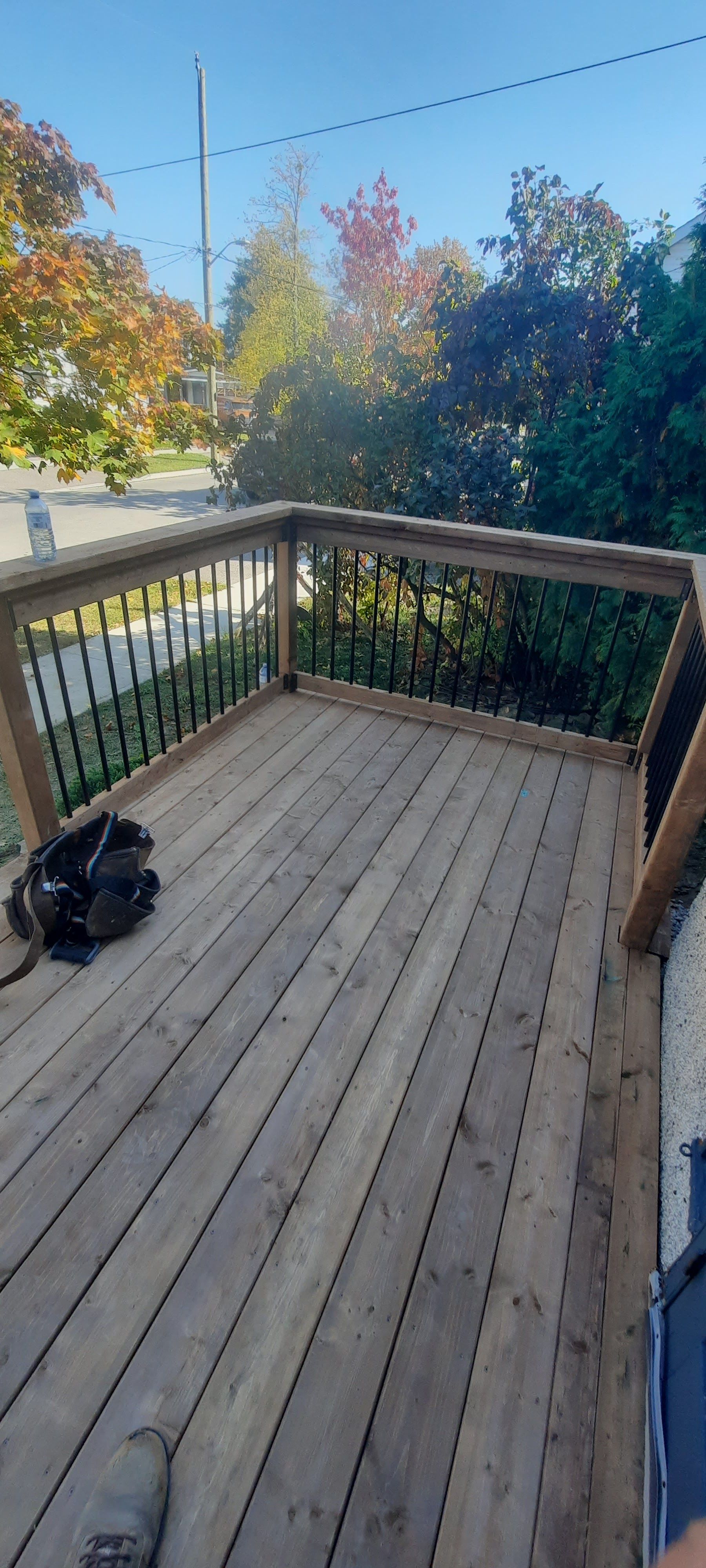 A wooden deck with a black backpack, overlooking trees and a bright blue sky.