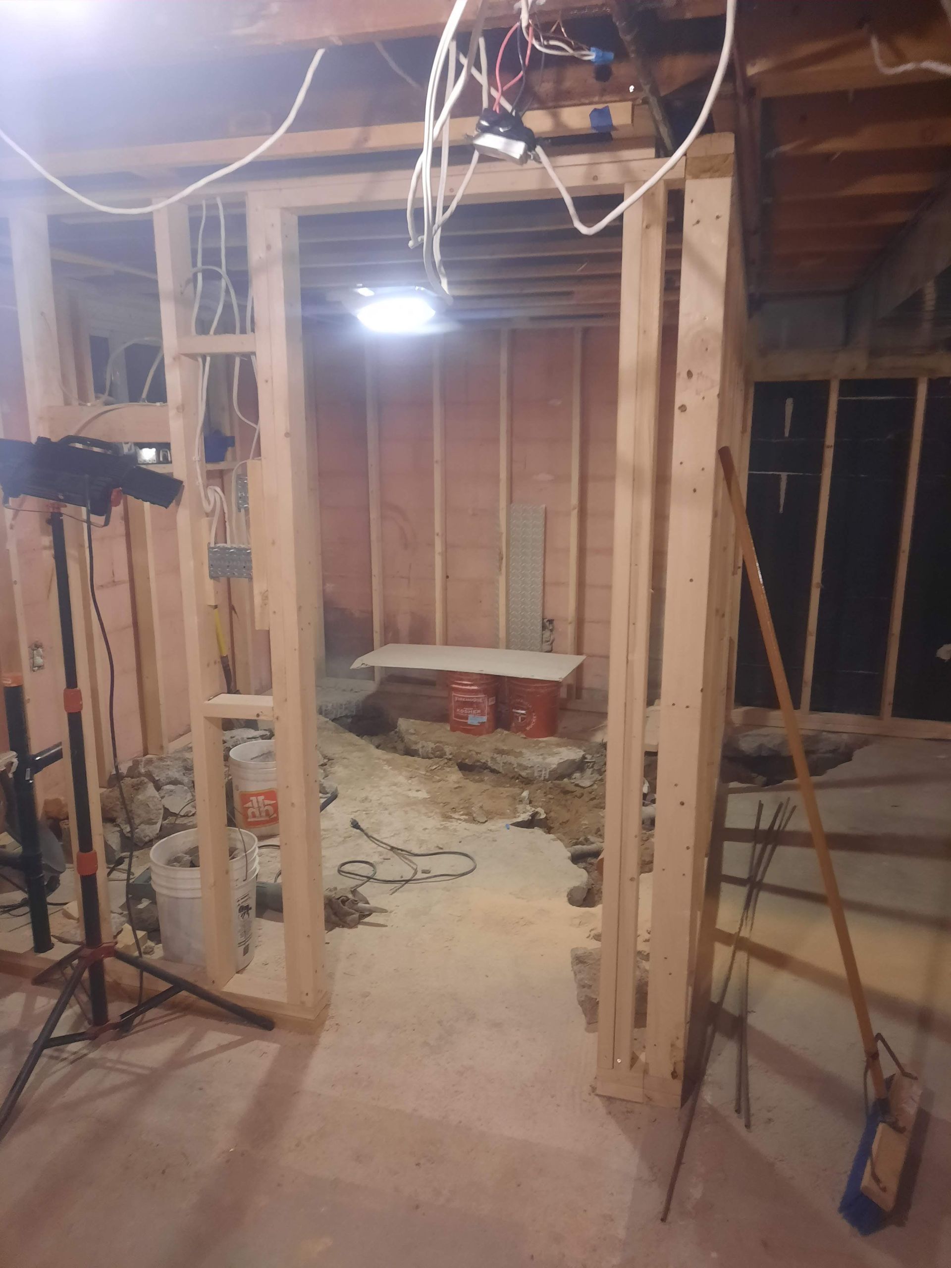 Construction site interior: wooden studs frame a doorway, bare concrete floor, unfinished walls.
