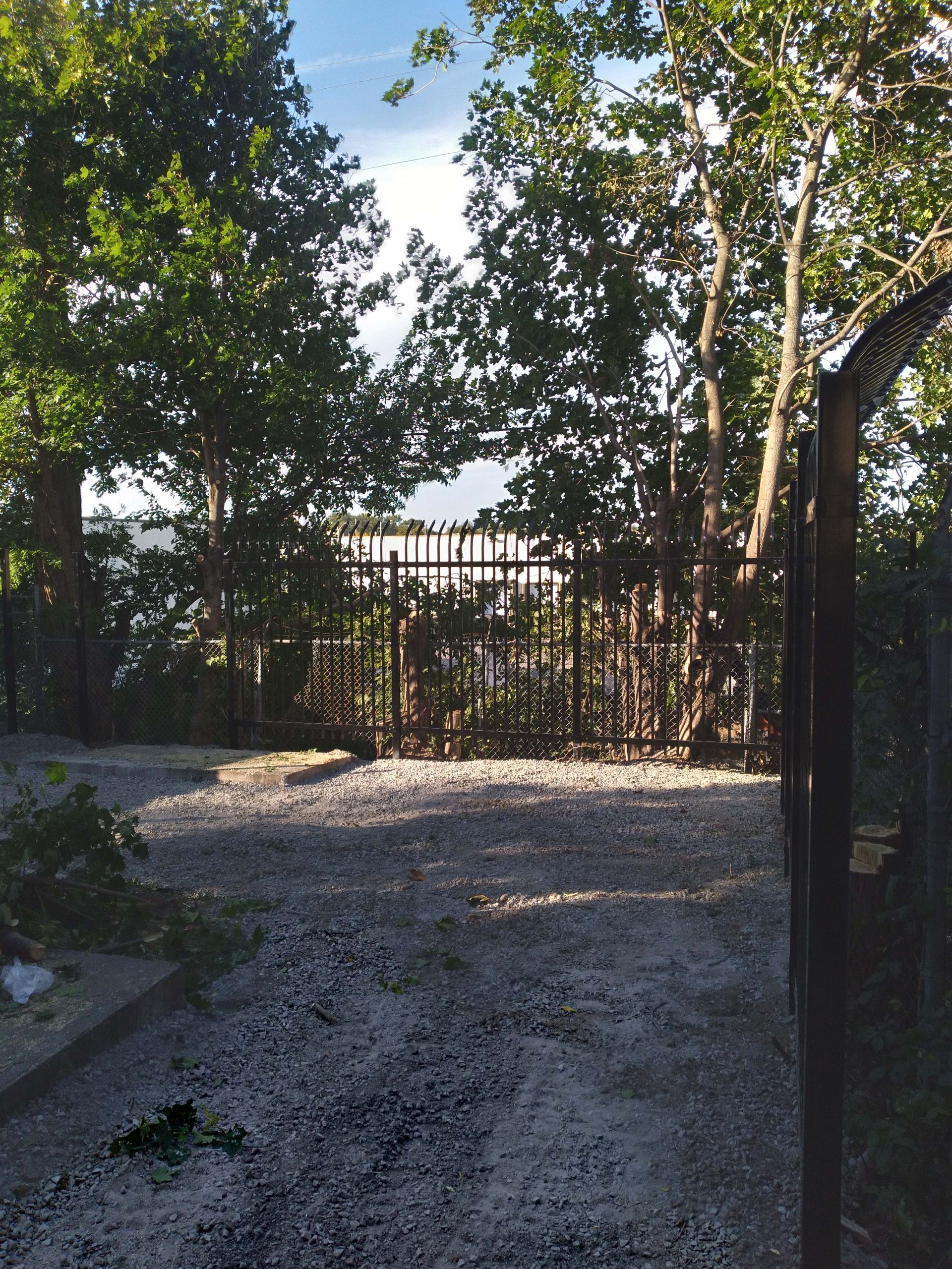 Gravel path leading to a fence gate, trees on either side, overcast sky visible.